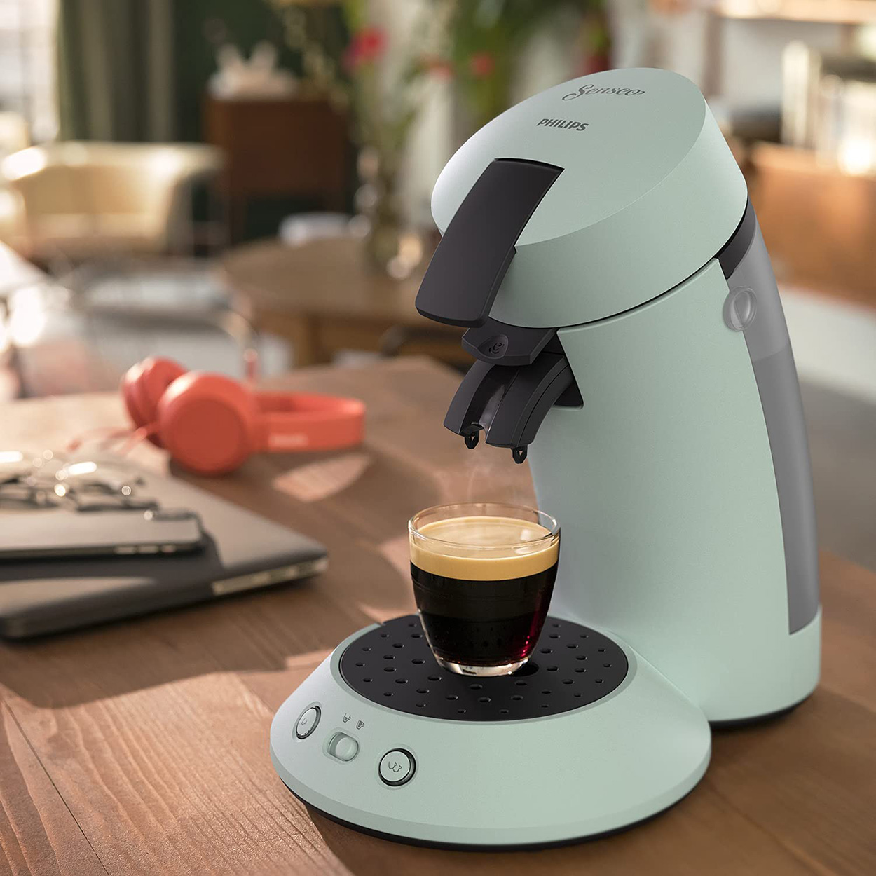 Minzgrüne Philips Senseo Kaffeemaschine mit einer Tasse Kaffee auf einem Holztisch mit Kopfhörern.