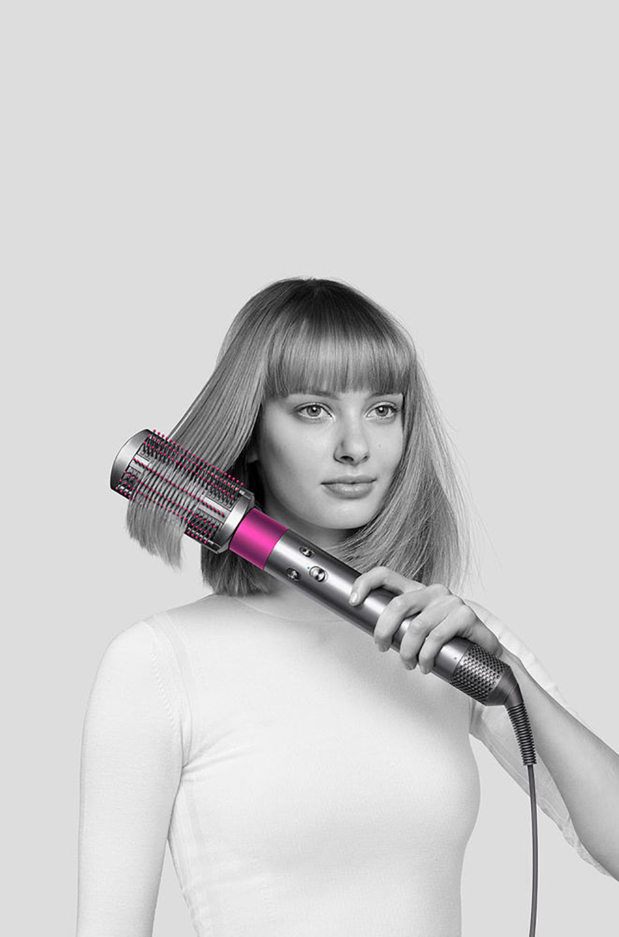 Frau benutzt einen Dyson Haarstyler. Das Werkzeug ist silber und rosa. Schwarz und weiß.