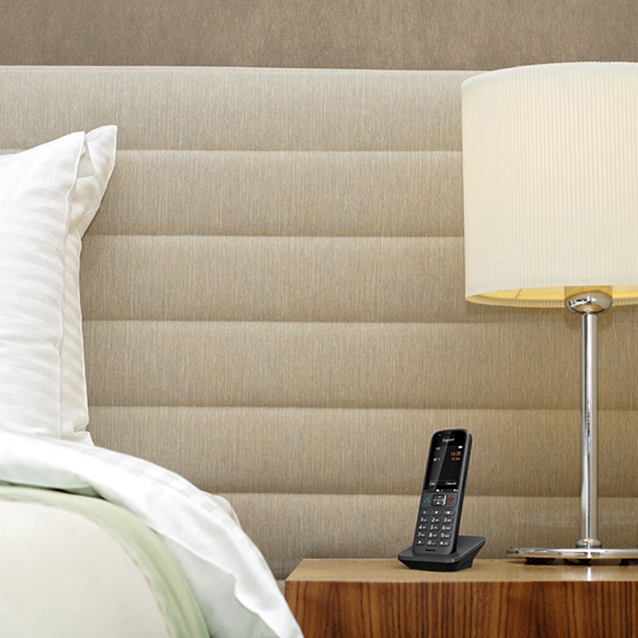 Scena sypialni. Łóżko z białą poduszką, lampa na stoliku nocnym i telefon bezprzewodowy.
