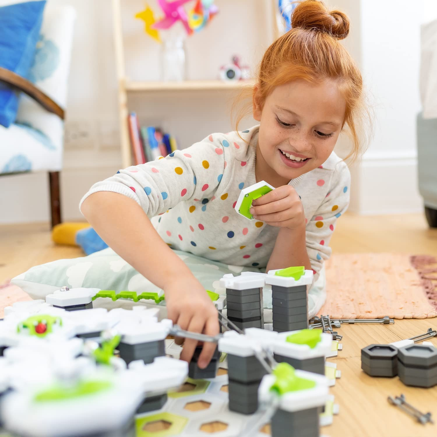 Una bambina gioca con un giocattolo su un tappeto, sorridendo.