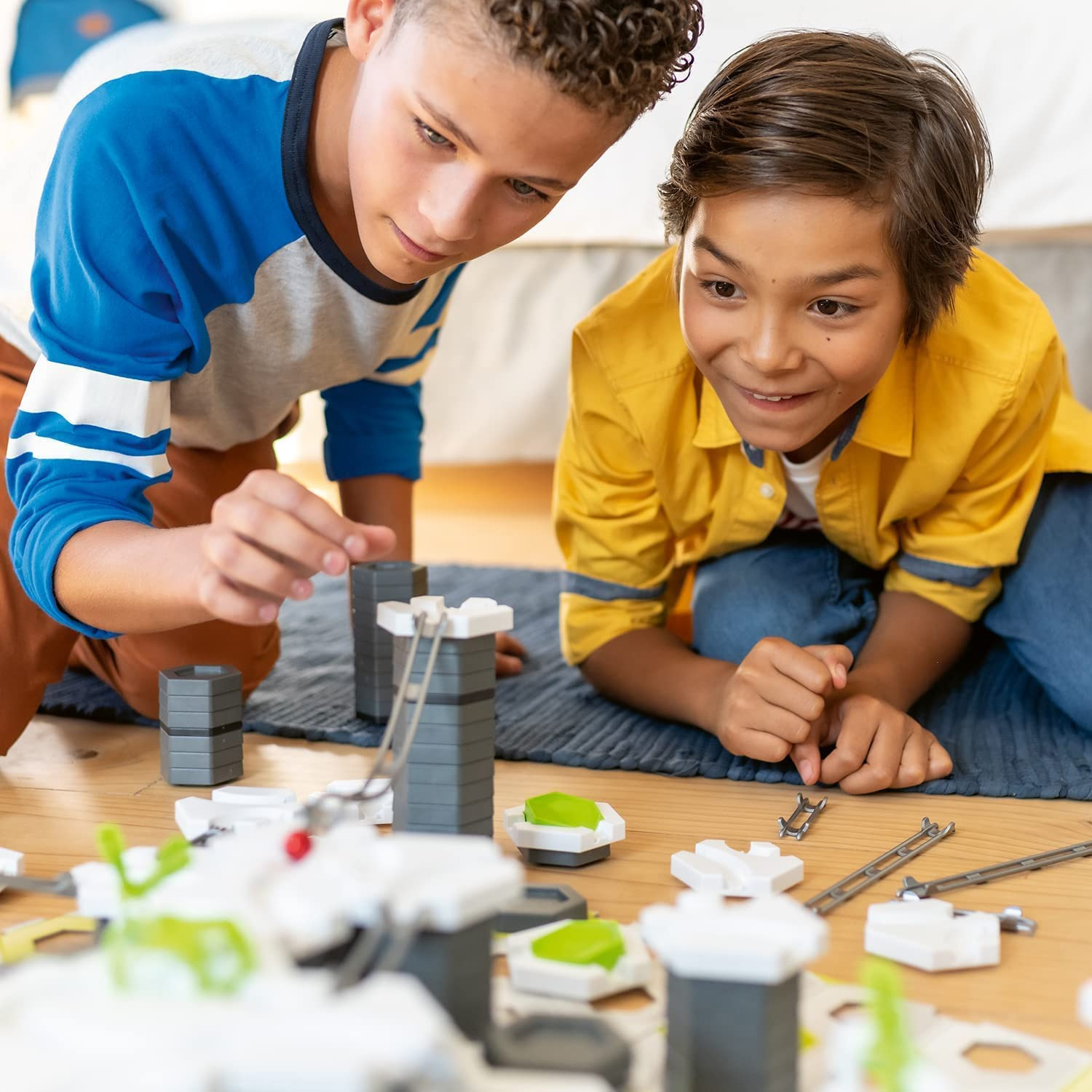 Due ragazzi che costruiscono con blocchi di giocattoli. Pavimento in legno, blocchi sparsi.