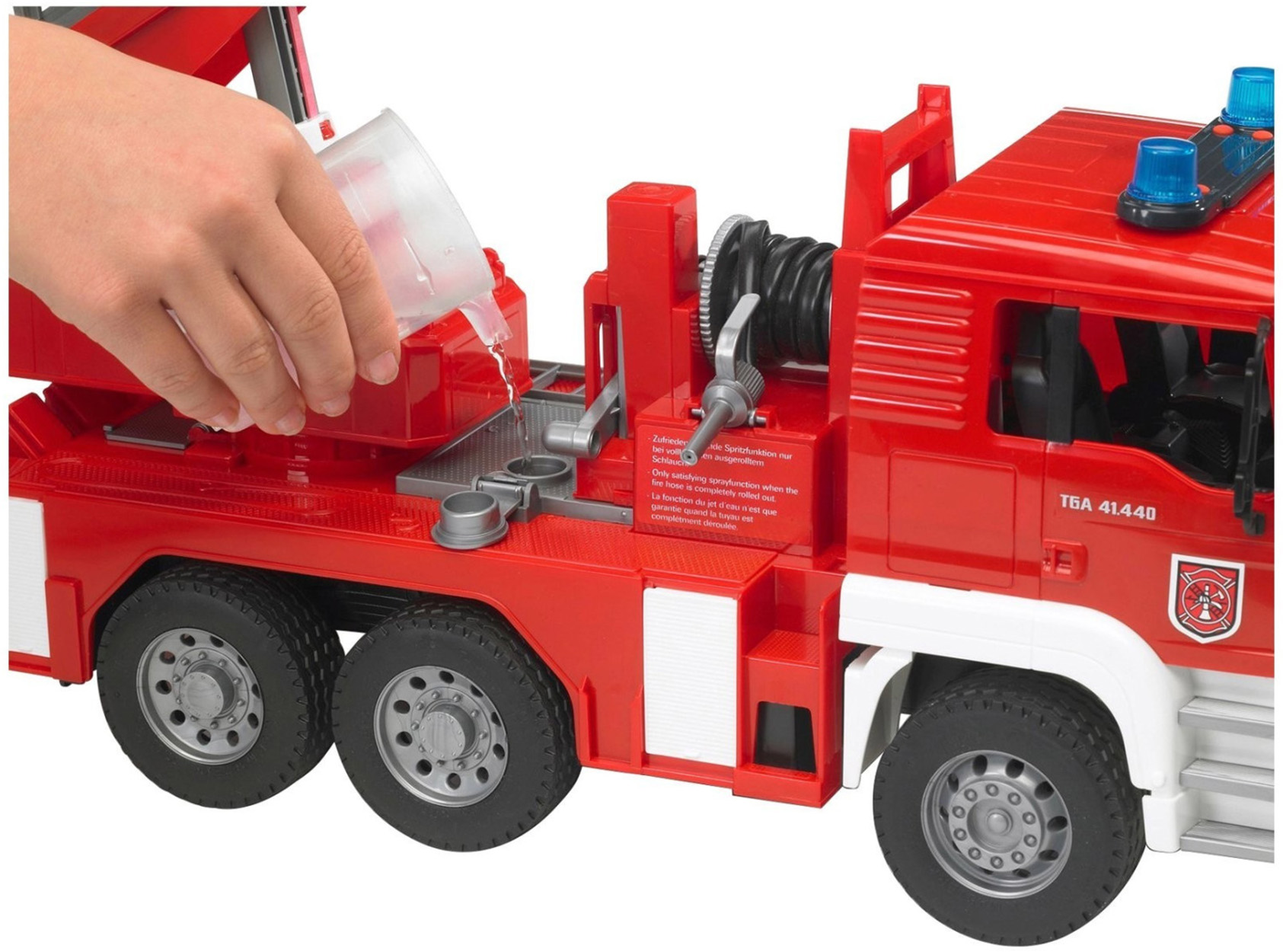 Ręka dziecka wlewa wodę do zabawkowego wozu strażackiego, czerwono-białego.
