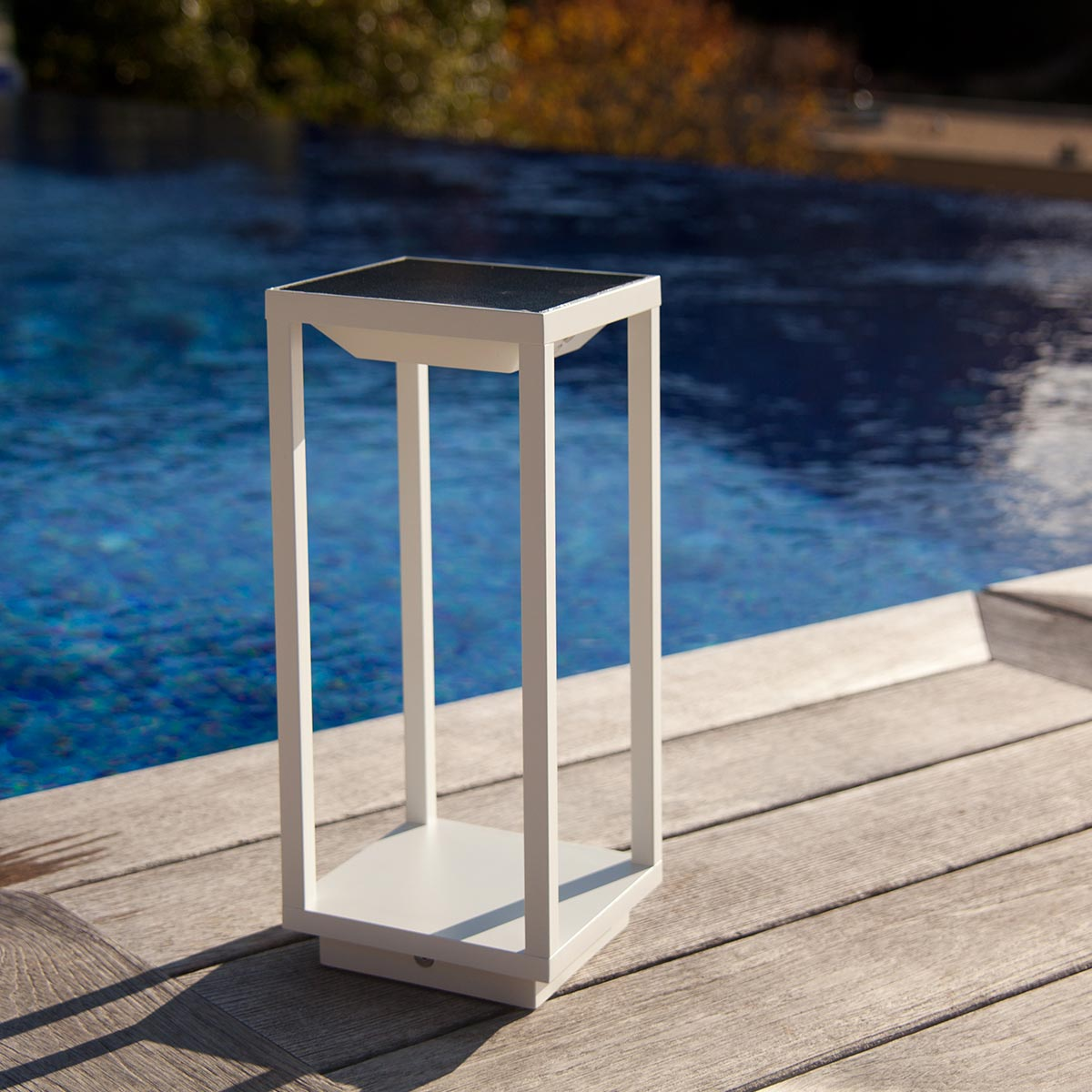 Weiße Laterne an einem Pool. Sie hat einen schwarzen Deckel und steht auf einem Holzdeck.