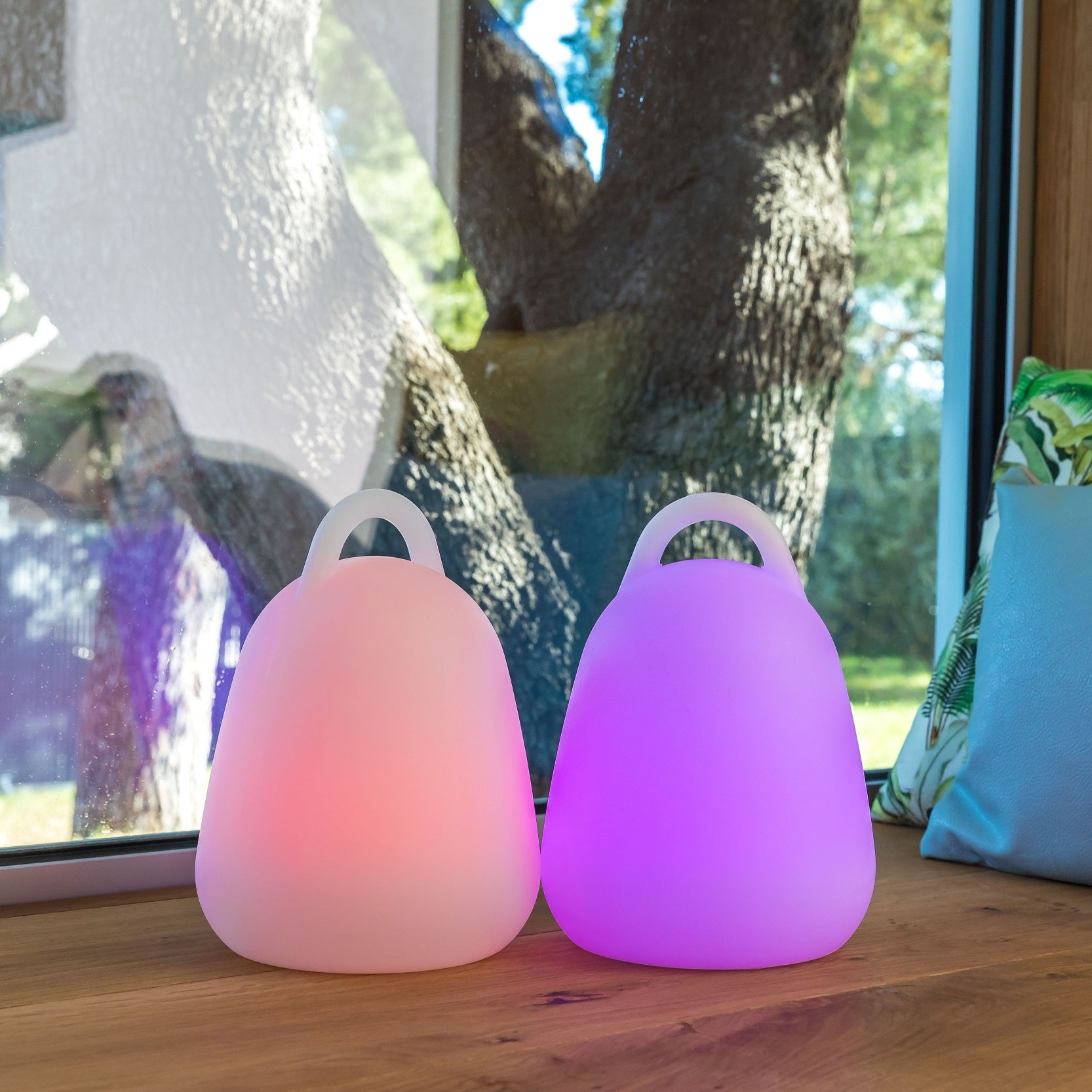 Zwei beleuchtete, tropfenförmige Lampen, eine rosa, eine lila, auf einer Holzoberfläche.