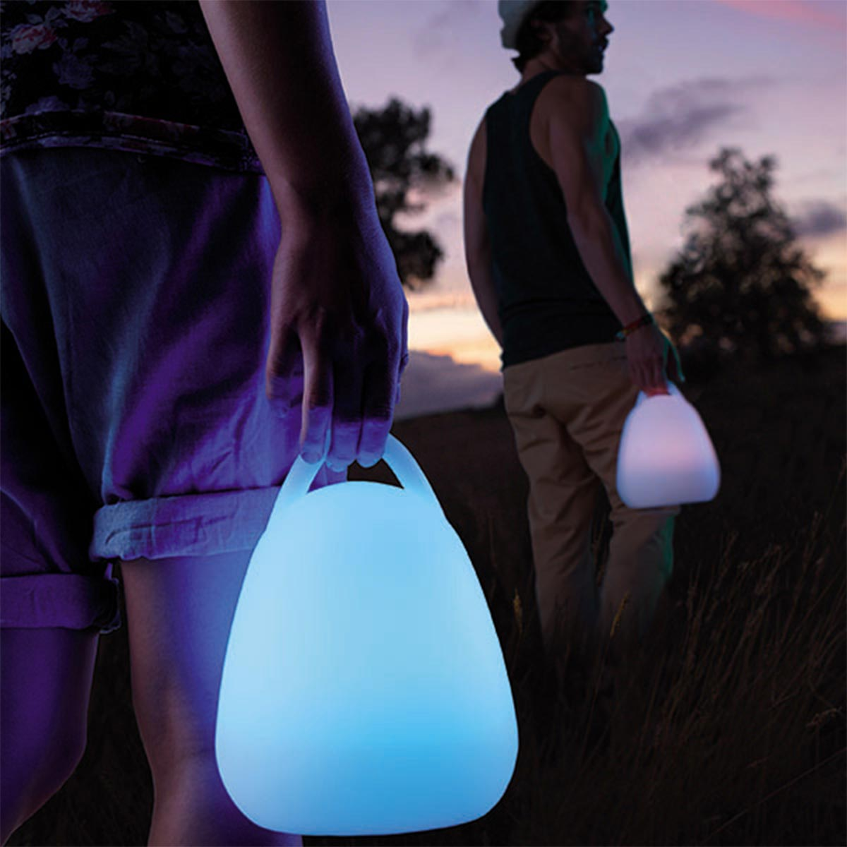 Zwei Personen halten beleuchtete blaue Lampen auf einem Feld in der Dämmerung. Eine im Vordergrund.