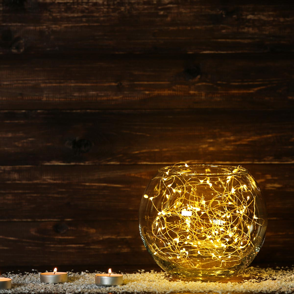 Eine Glasschale mit Lichterketten, Kerzen auf dem Tisch, Holz Hintergrund.