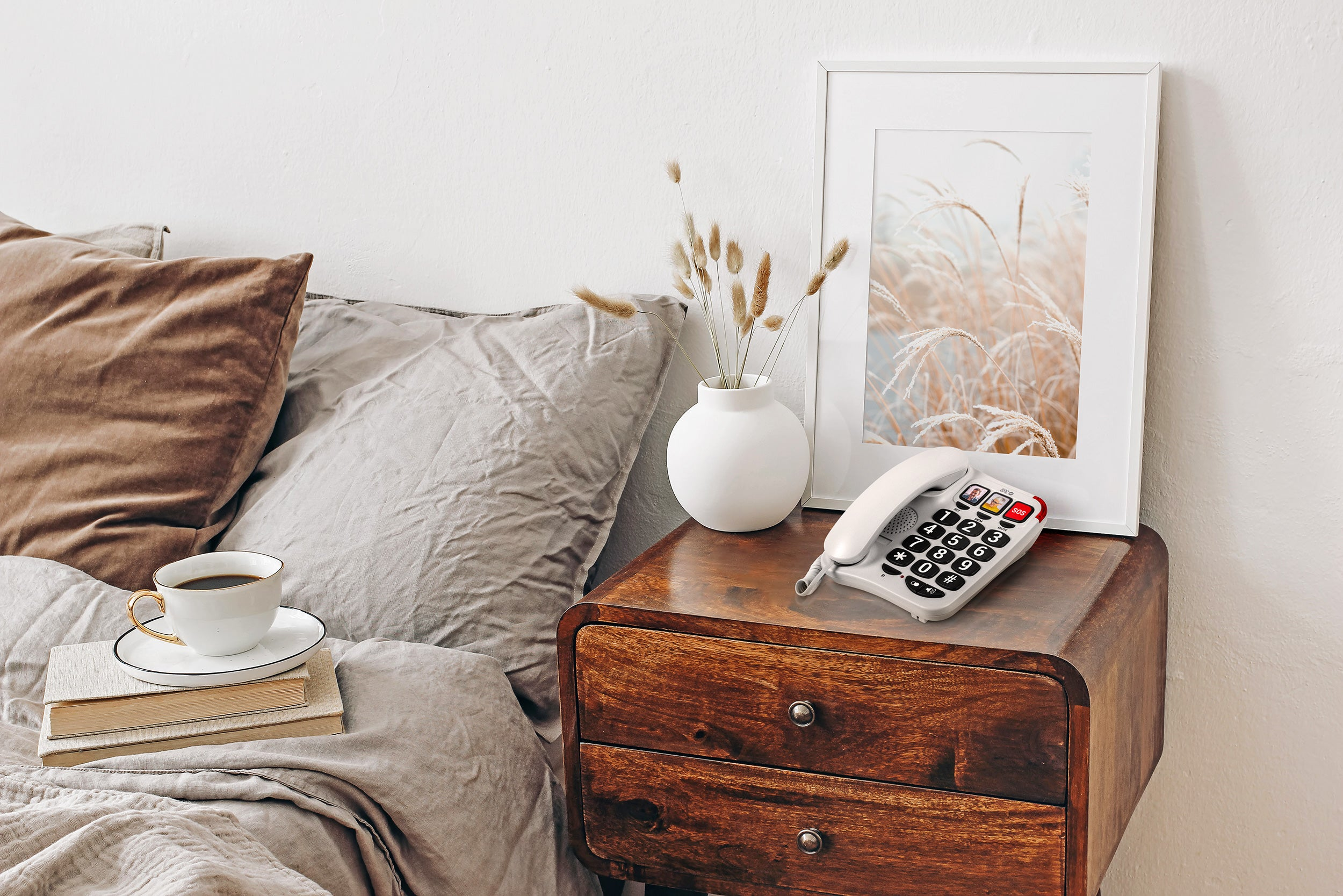 Comodino con telefono bianco, tazza di caffè, libri e una foto incorniciata.