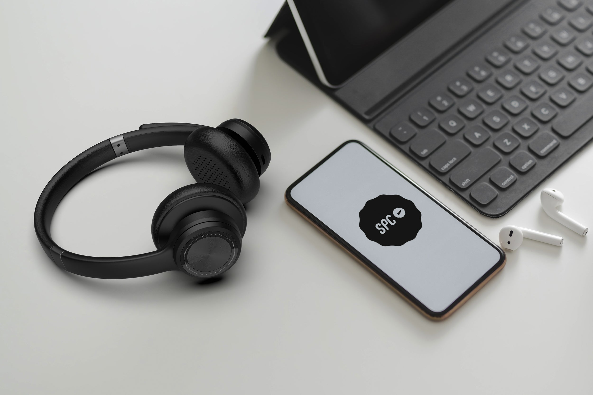 Cuffie over-ear, smartphone con logo SPC e auricolari wireless su una superficie bianca.