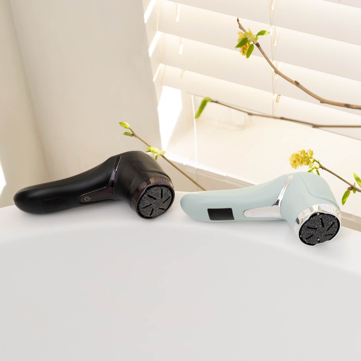 Dwa elektryczne pilniki do stóp, czarny i jasnoniebieski, na białej powierzchni.