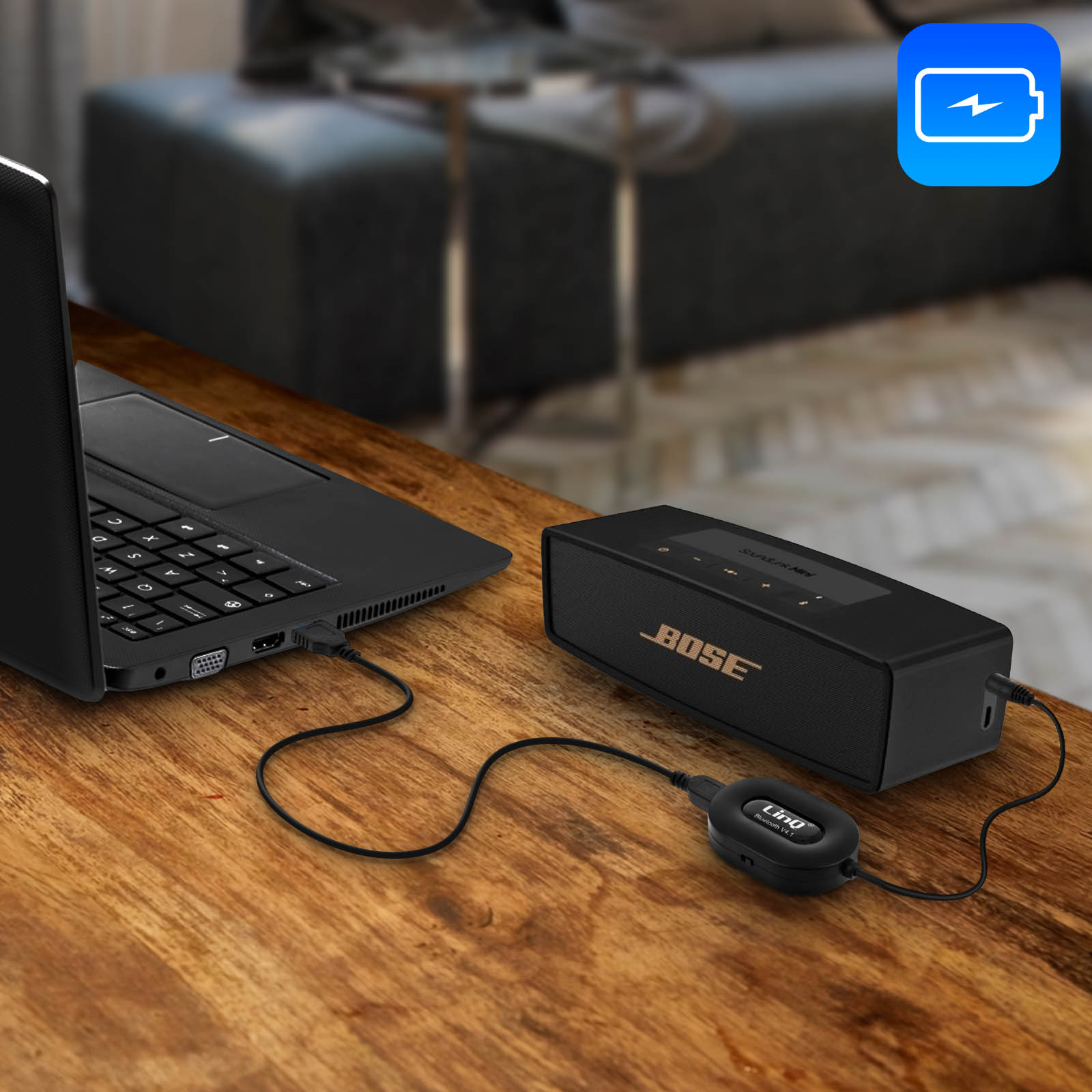 Laptop in carica altoparlante. Altoparlante nero con logo Bose. Tavolo in legno. Icona batteria blu.