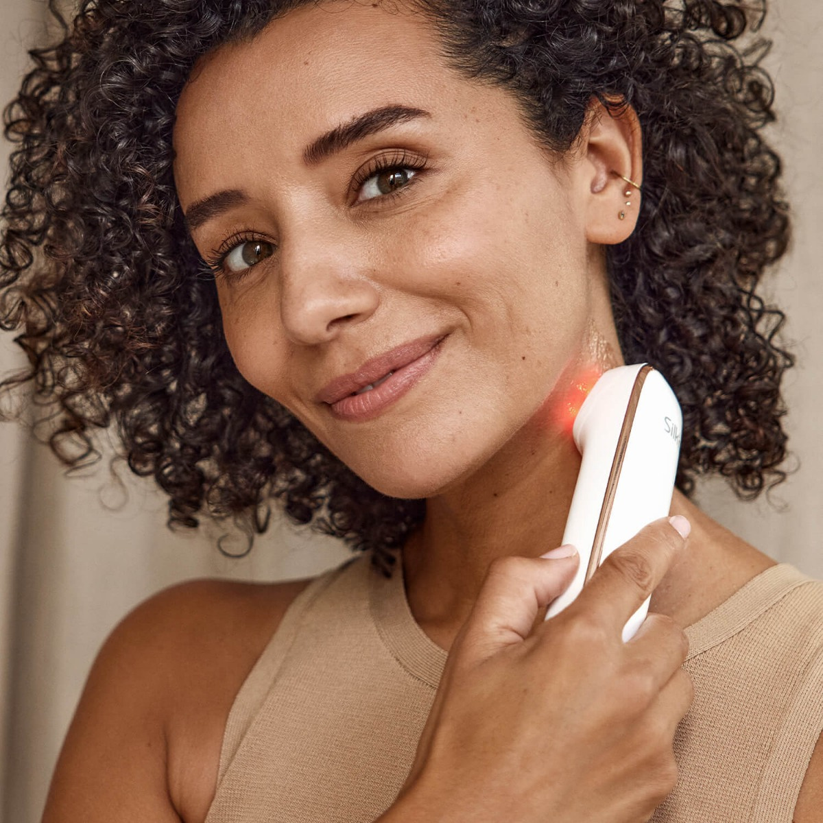 Femme tenant un masseur facial blanc près du cou, souriante.