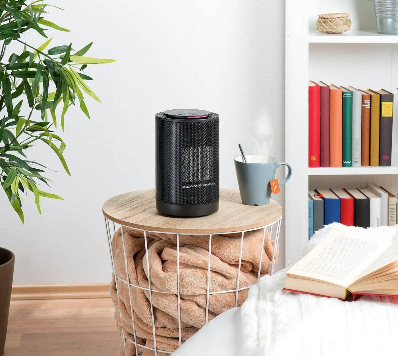 Schwarzer elektrischer Heizlüfter auf einem Holztisch, mit Tasse und Buch.