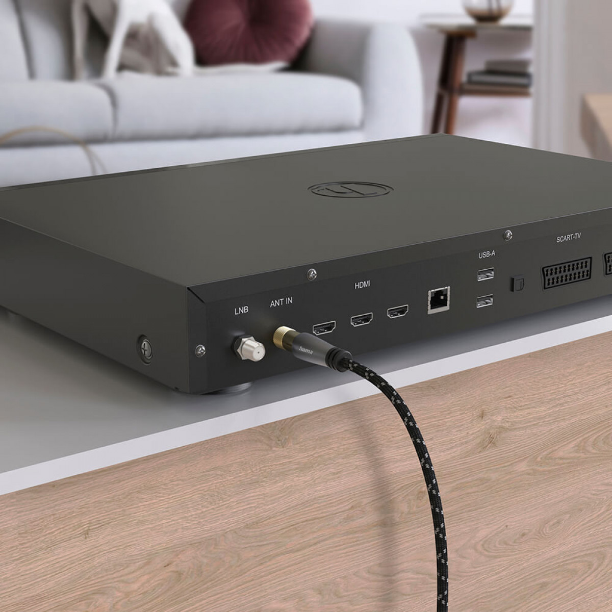 Czarne urządzenie z kilkoma portami, podłączone do kabla, na białym stole z sofą w tle.