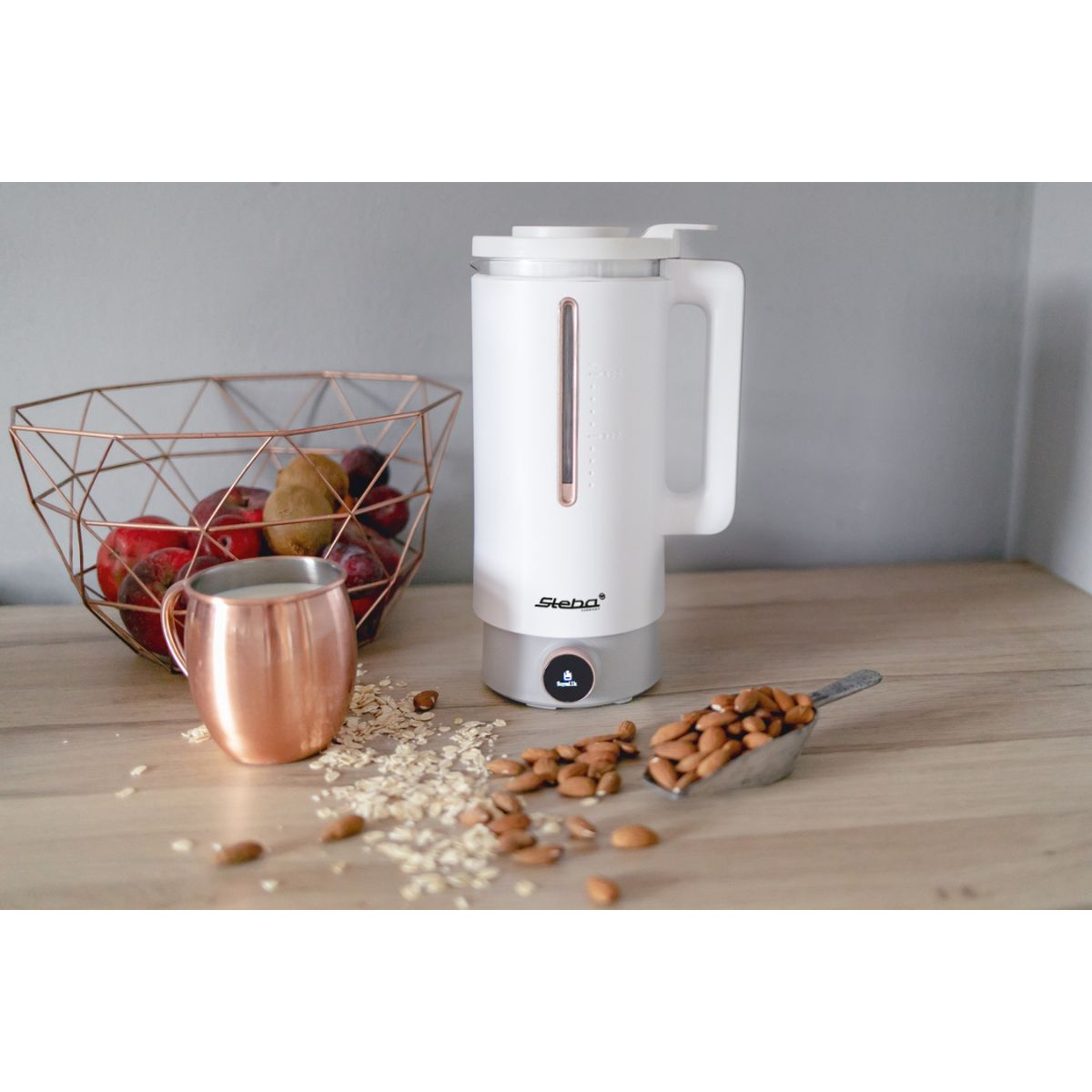 Ein weißer Mixer mit Mandeln und Früchten. Es gibt einen Kupferbecher und einen Drahtkorb.