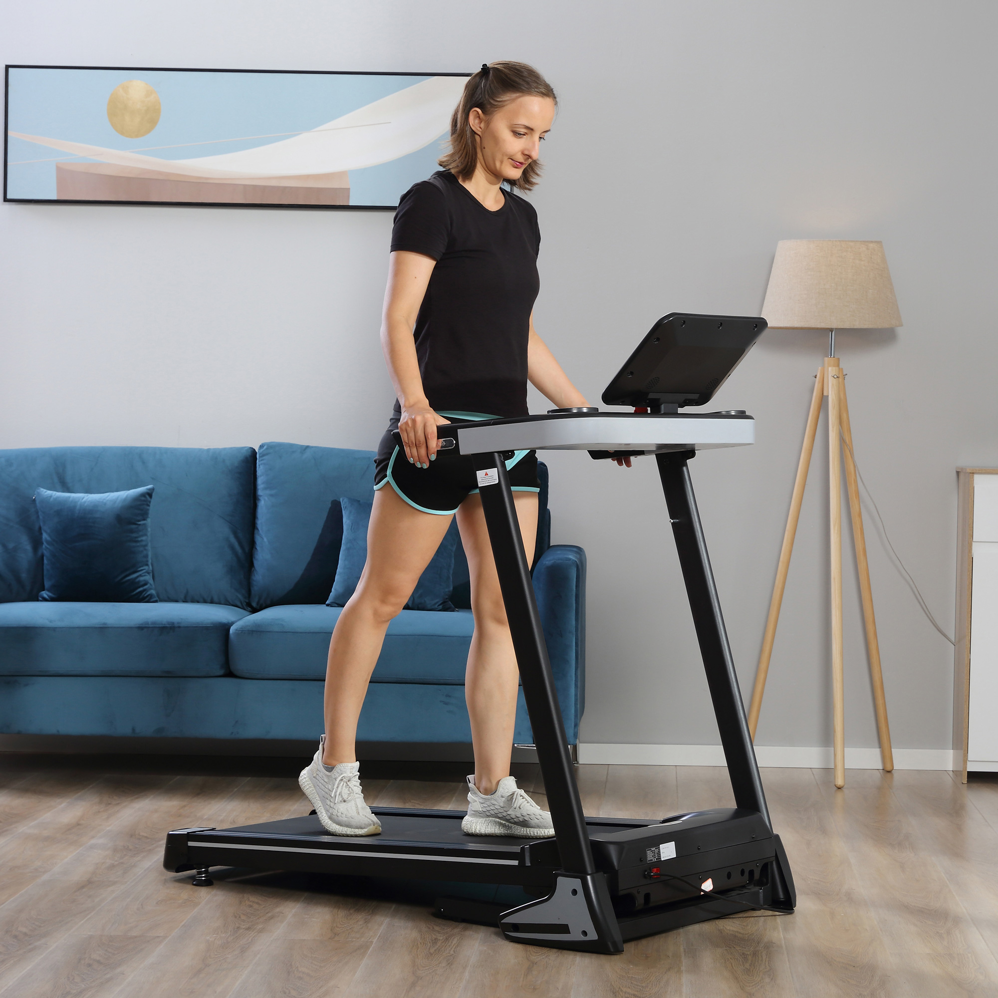 Donna su un tapis roulant in una stanza. Divano blu, lampada e altri mobili sullo sfondo.