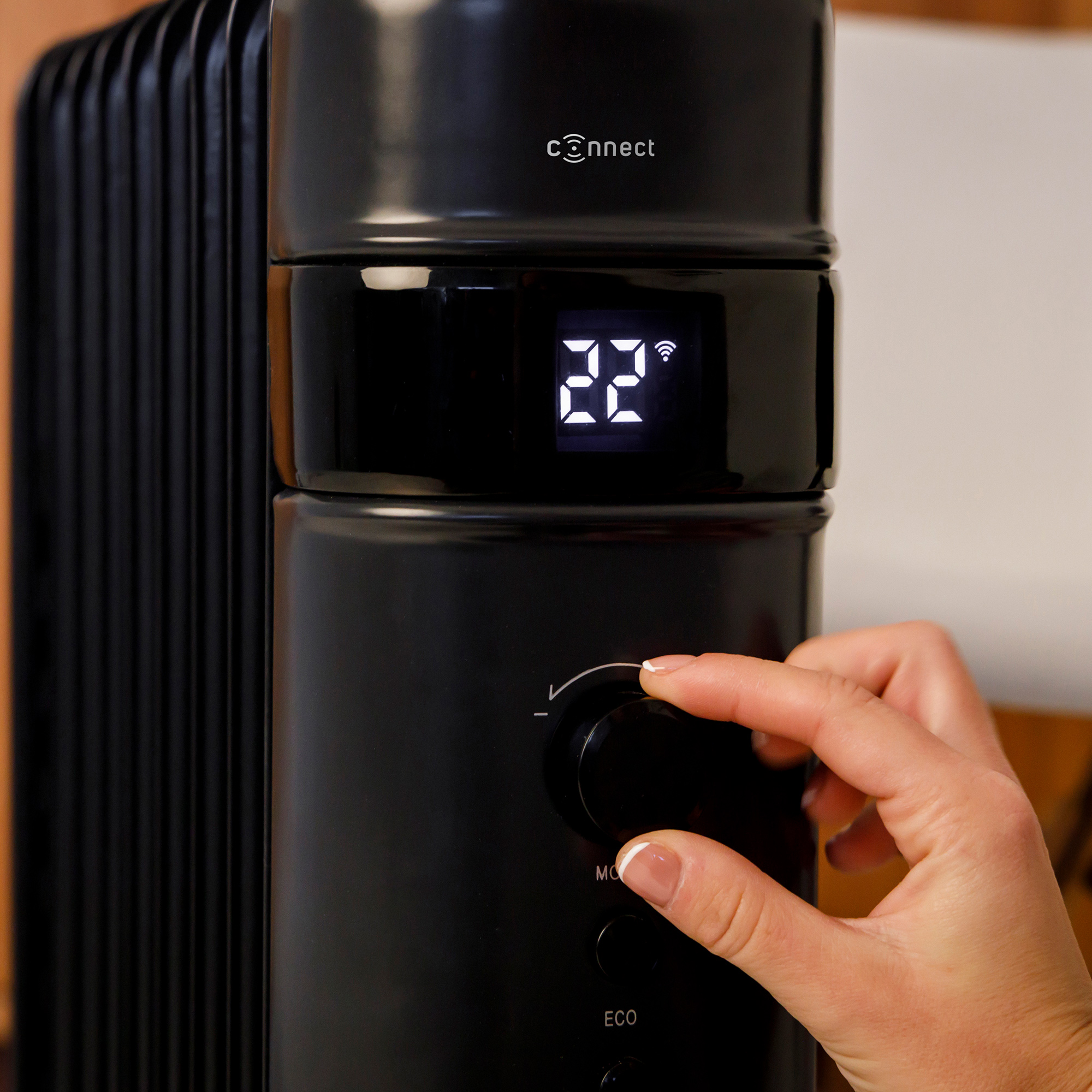 Una mano ajustando el dial de temperatura en un radiador negro. La pantalla digital muestra la temperatura.