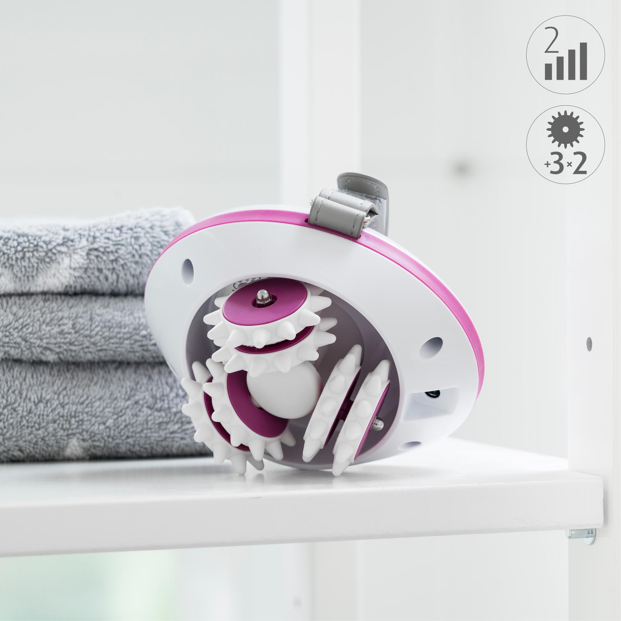 White and pink massage device on a shelf. Grey towels in the background.
