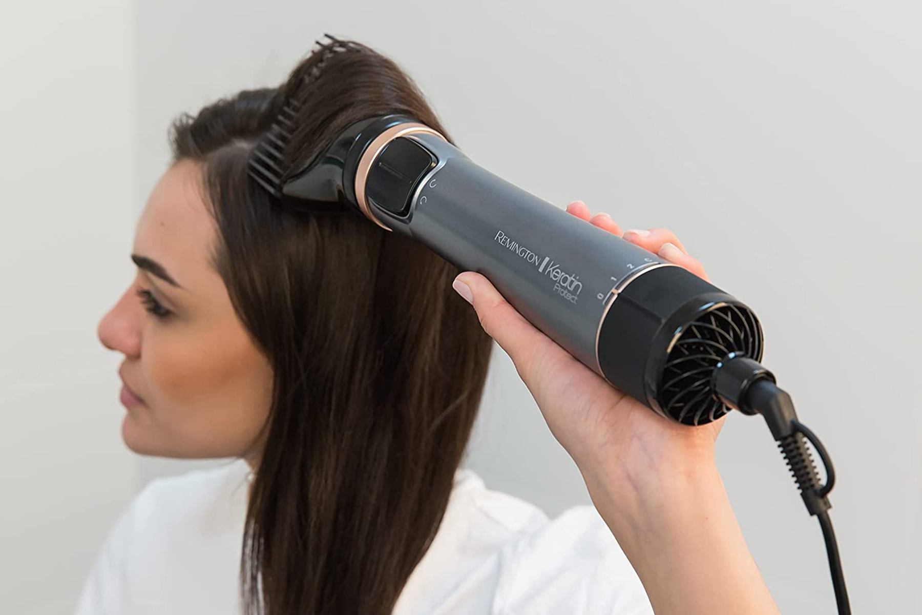 Una donna usa un asciugacapelli grigio su capelli scuri. Sfondo bianco.