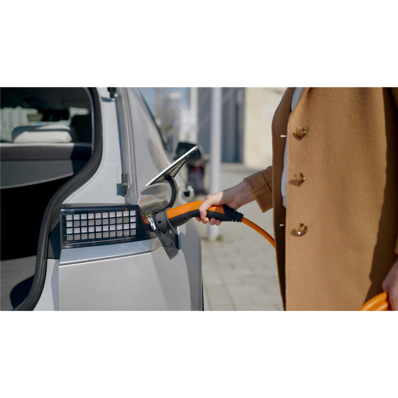 Eine Person, die ein orangefarbenes Ladekabel in ein silbernes Elektroauto steckt.
