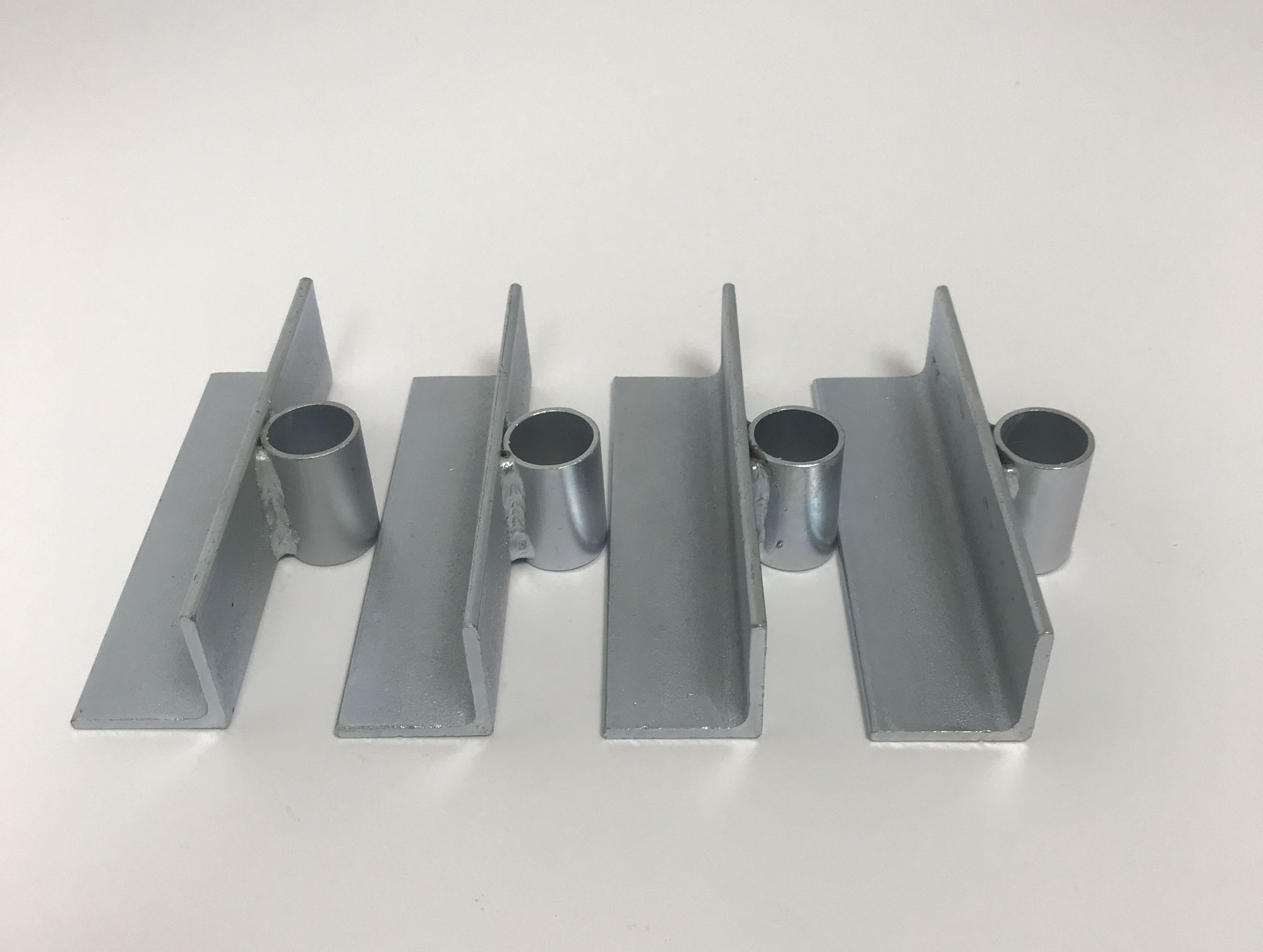 Vier silberne Metallhalterungen mit U-förmigem Querschnitt, jeweils mit einem zylindrischen Ring, auf weißer Oberfläche.