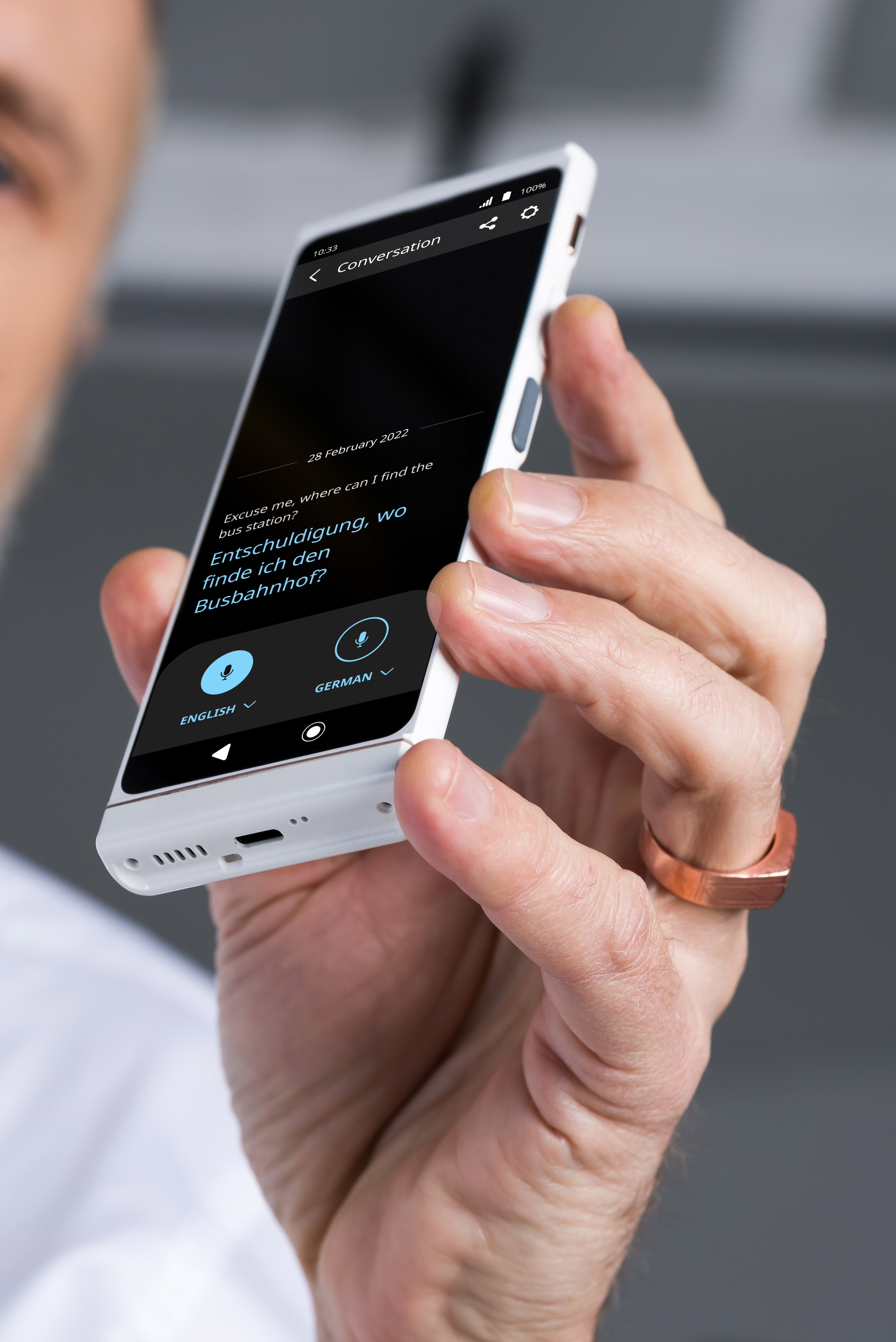 Ein Mann hält ein weißes Telefon, das eine Übersetzungs-App mit englischem und deutschem Text anzeigt.