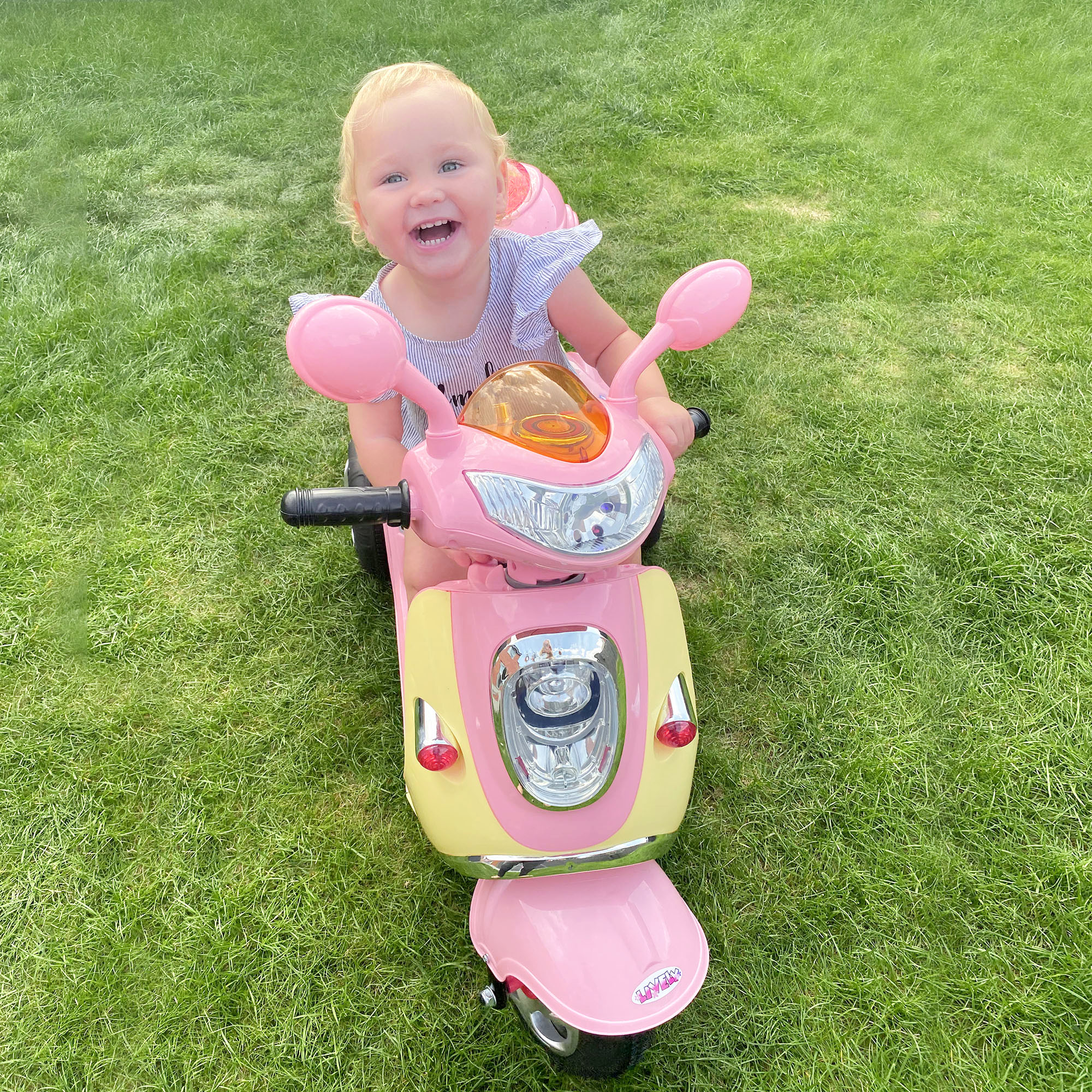 Un bambino allegro che guida uno scooter rosa e giallo sull'erba verde.