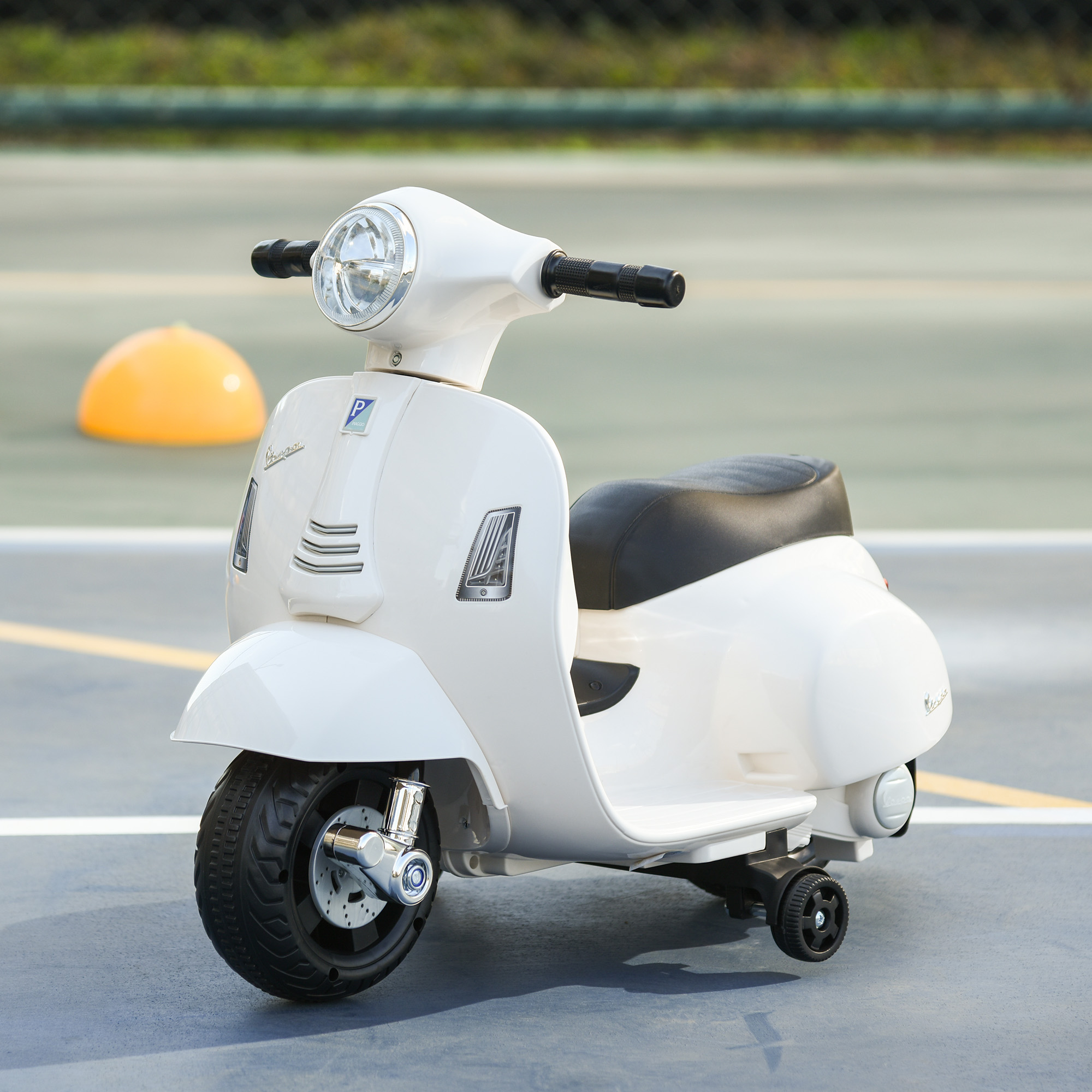 Scooter de juguete blanco con asiento y ruedas negras, sobre una superficie gris. Luz y logo visibles.