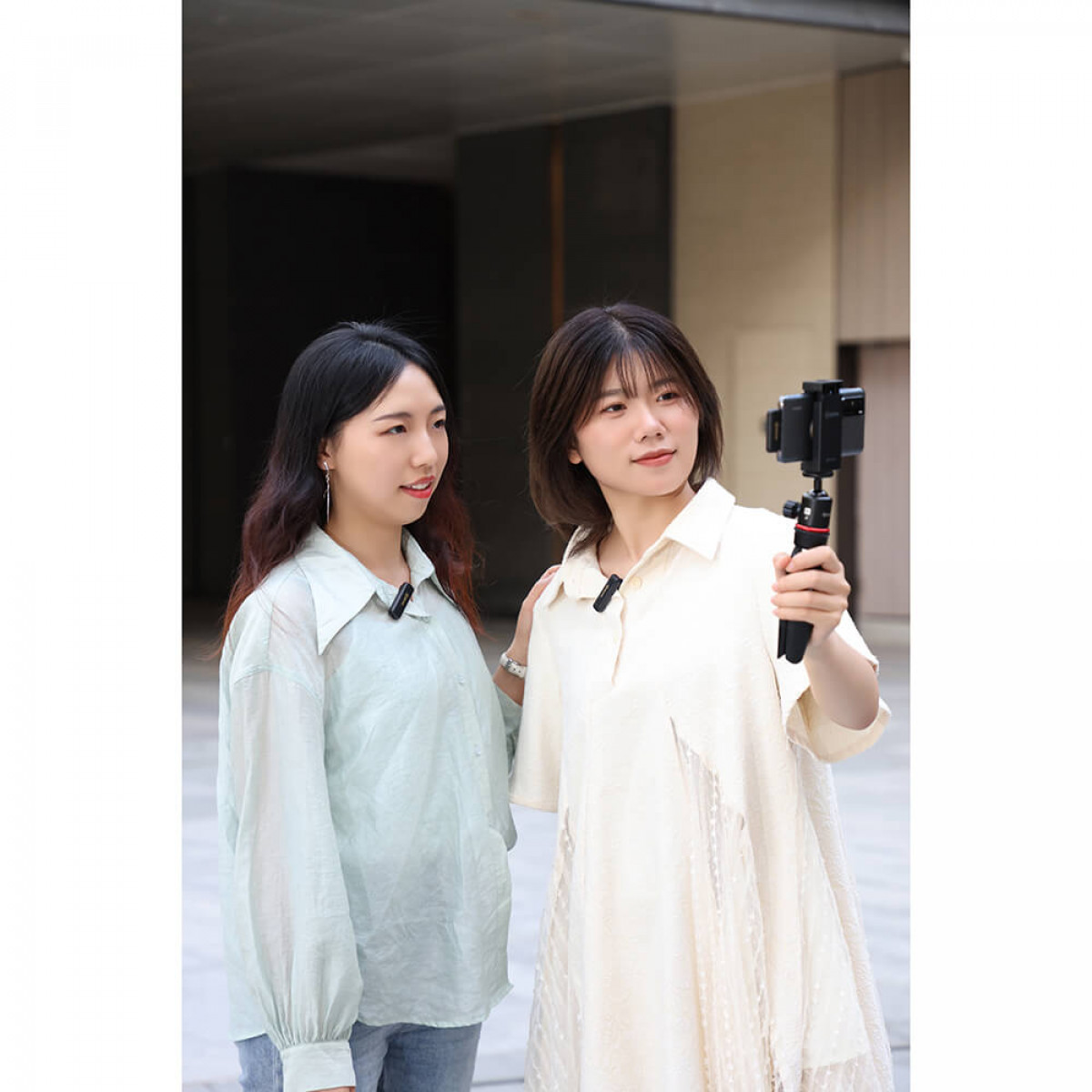 Twee vrouwen met dasspeldmicrofoons buiten. Eén houdt een telefoon op een gimbal, lichte achtergrond.