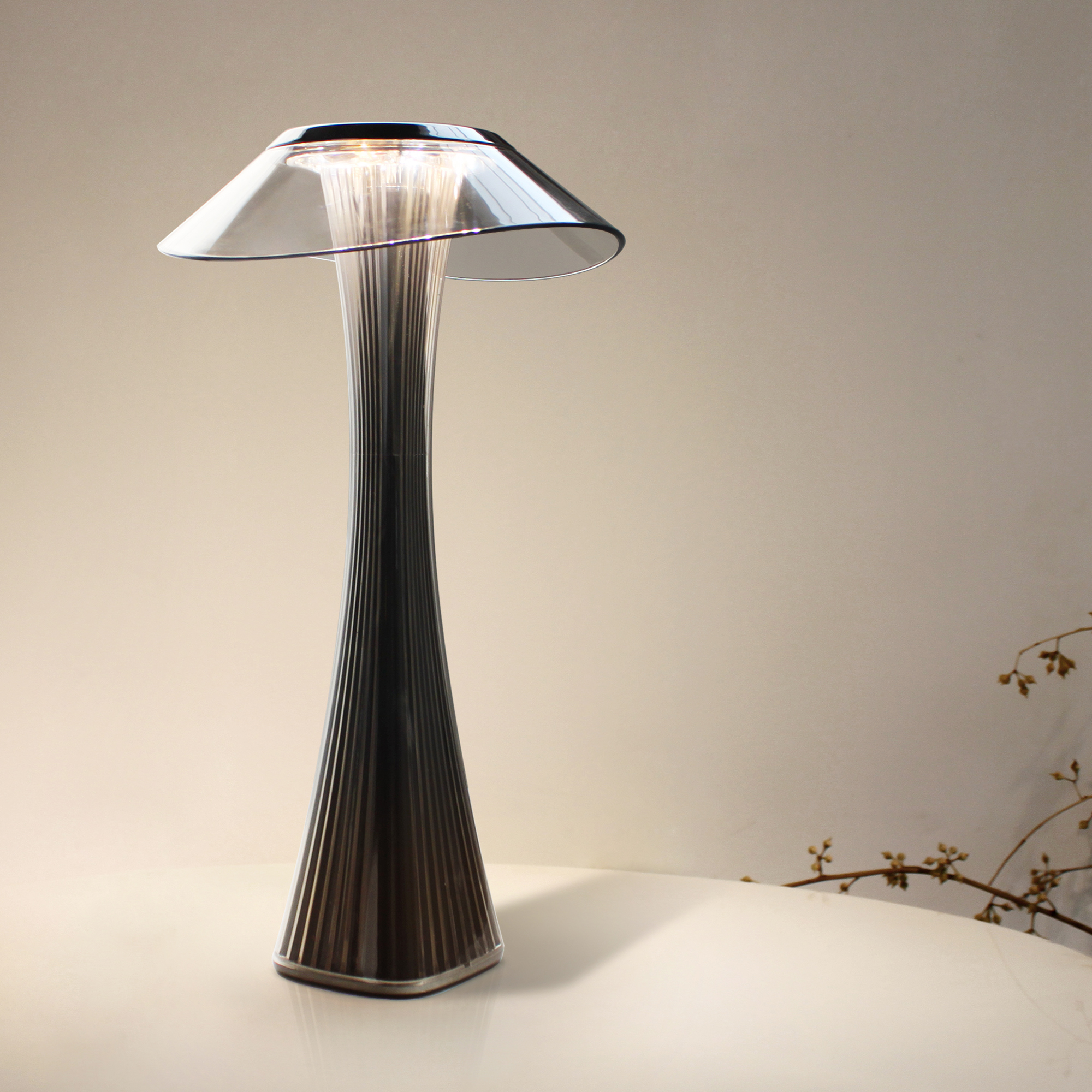 Moderne Tischlampe mit schwarzem Fuß und transparentem Schirm, auf einem weißen Tisch.