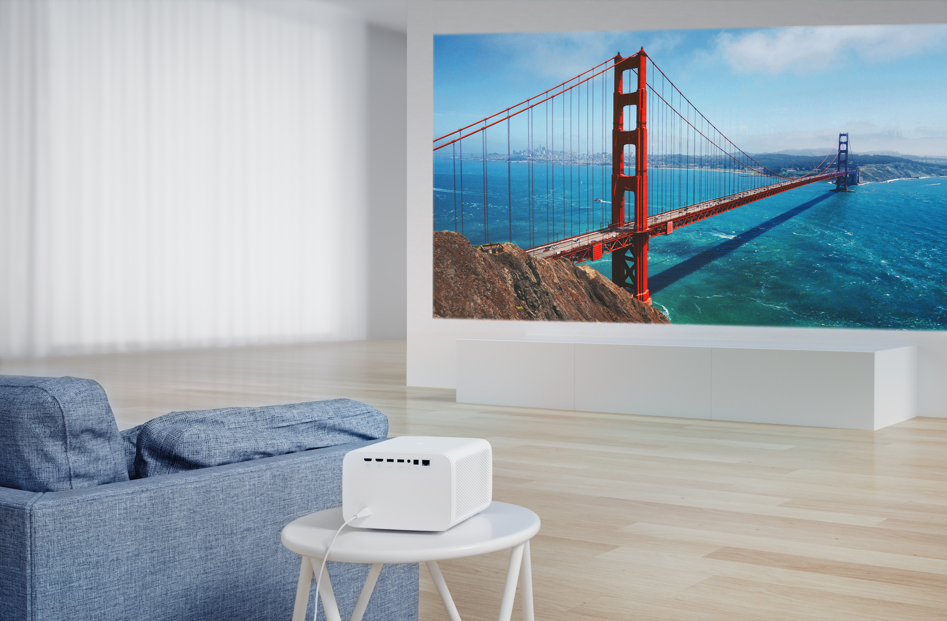 Proyector blanco en mesa, proyectando el Golden Gate, sofá azul a la izquierda.