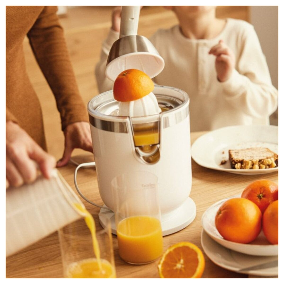 Una persona exprimiendo media naranja en un exprimidor eléctrico, el jugo fluye a un vaso.