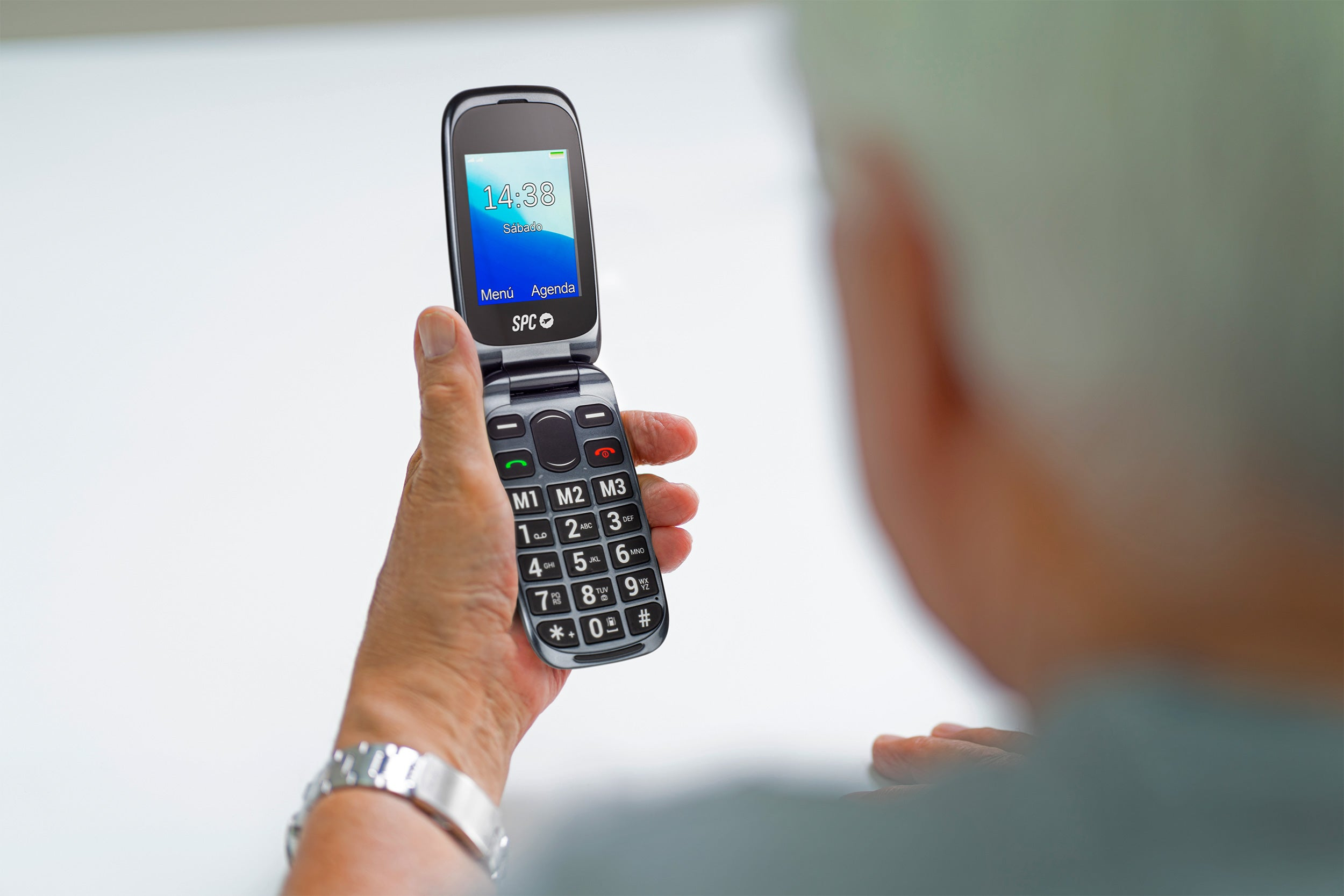 Una persona sosteniendo un teléfono plegable que muestra la hora. El teléfono es negro con botones grandes.