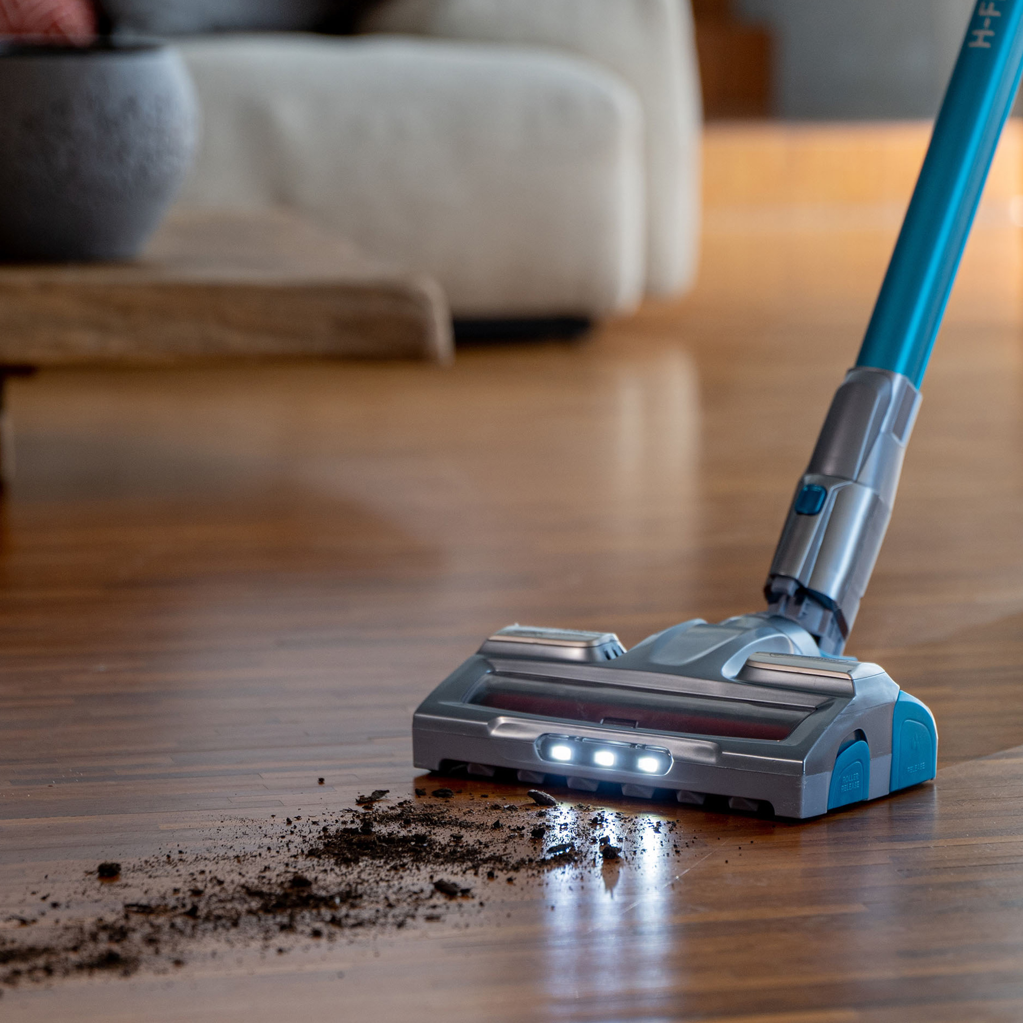 Cabezal de aspiradora limpiando un piso de madera. Suciedad y polvo son visibles en el suelo.