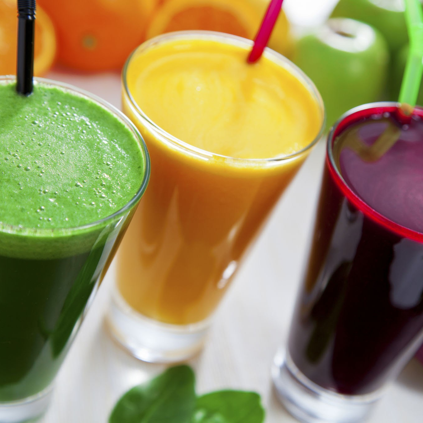 Tres vasos de jugo: verde, amarillo y rojo, con pajitas y fruta en el fondo.