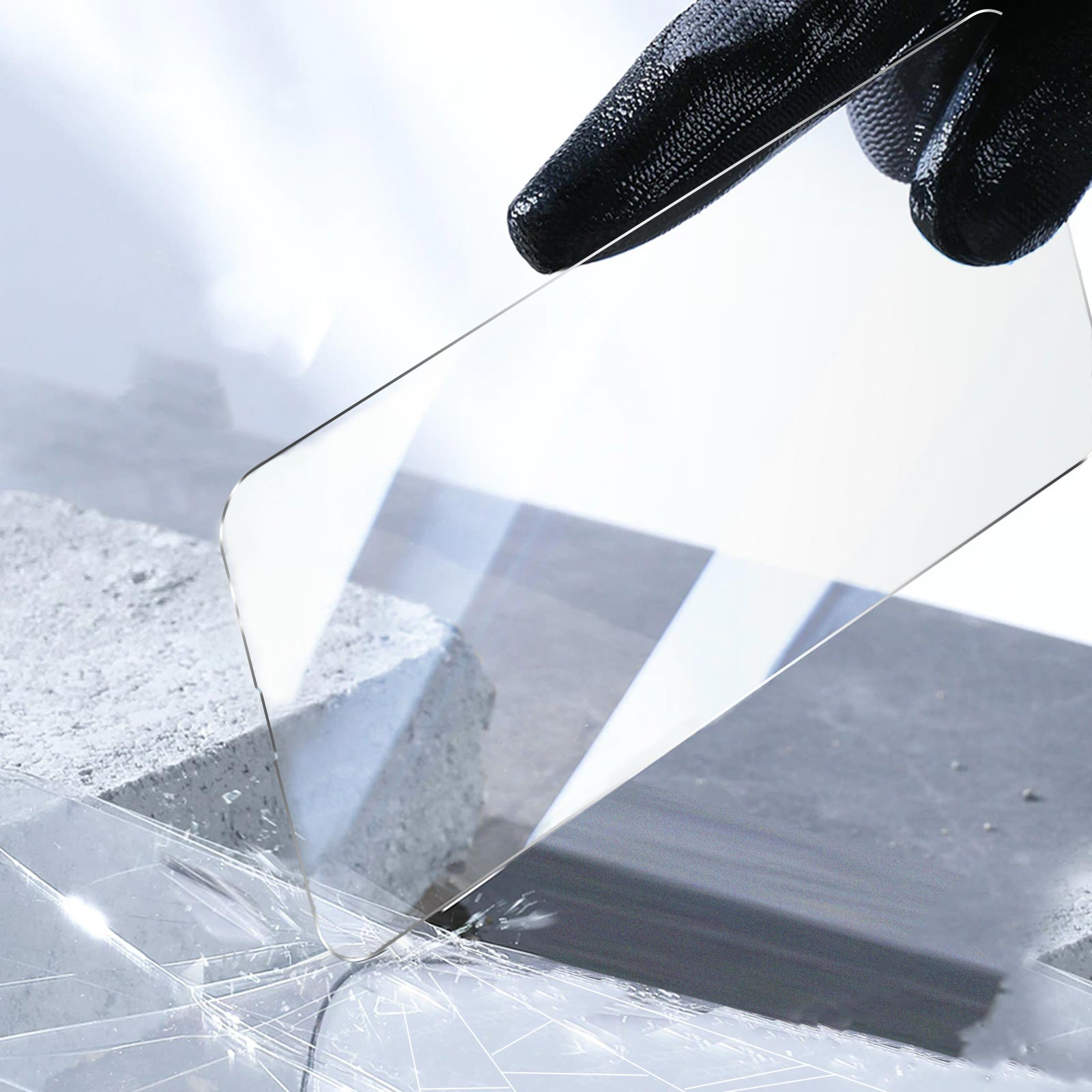 Un protecteur d'écran transparent est tenu au-dessus du béton. Une main gantée de noir le tient.