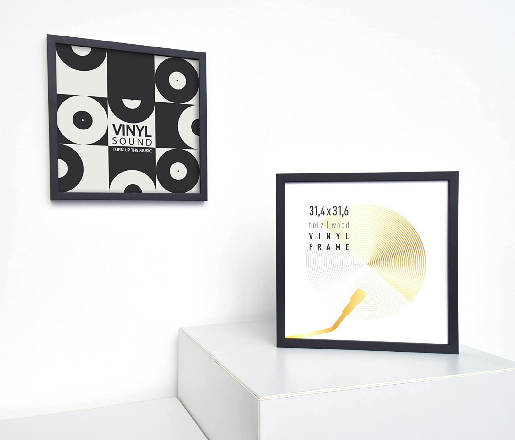 Zwei gerahmte Vinylplatten-Kunstwerke auf weißer Oberfläche. Eines hat ein Schwarz-Weiß-Design, das andere ein goldenes Plattendesign.