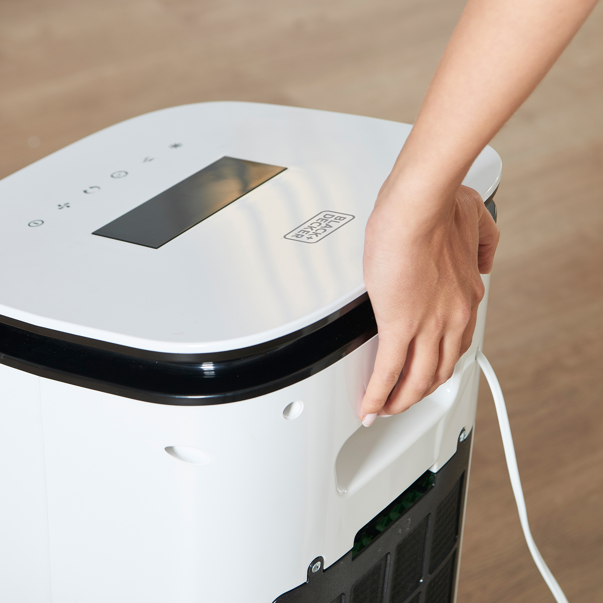 Una mano che afferra un purificatore d'aria bianco Black + Decker. Sono visibili colori bianco e grigio.