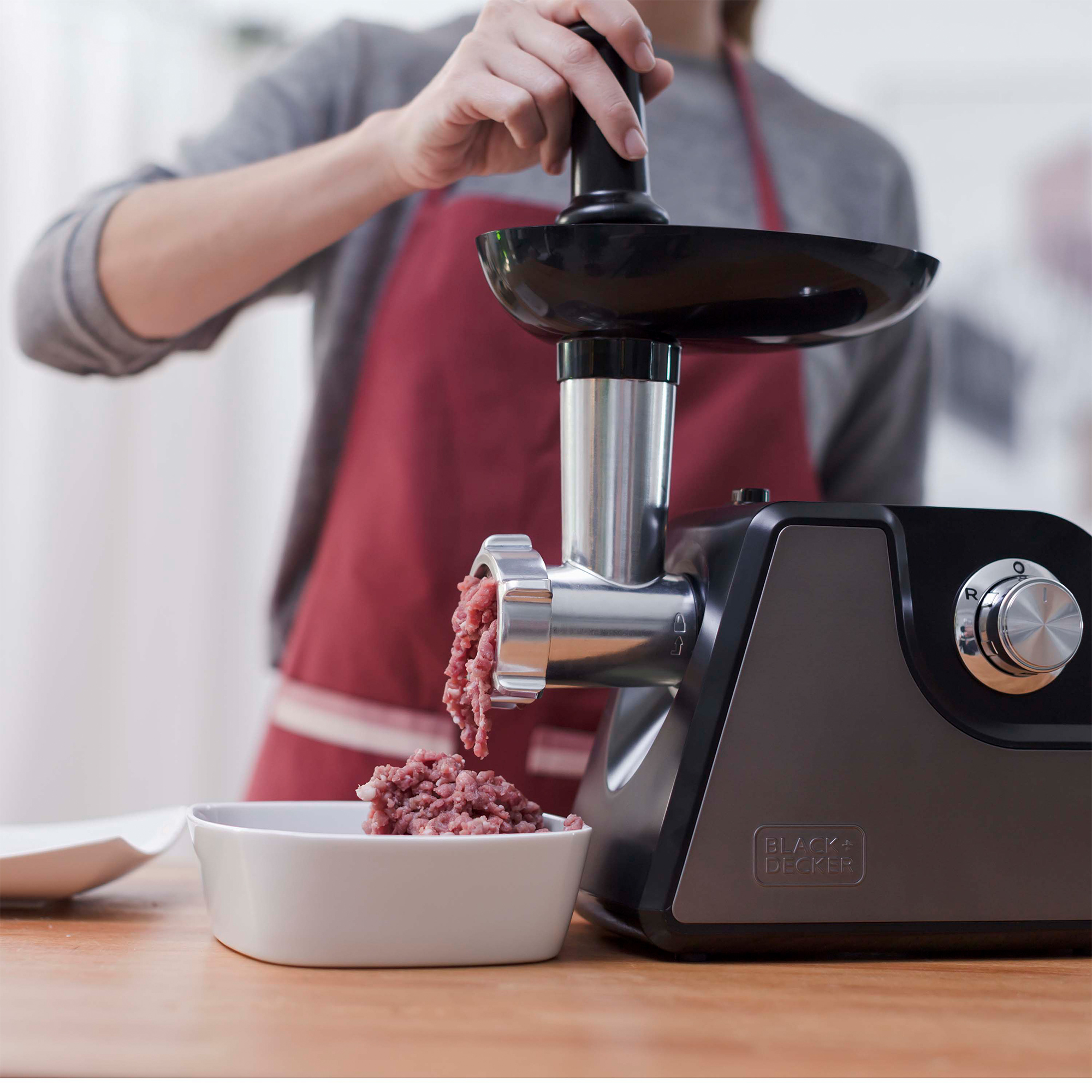 Osoba używająca maszynki do mielenia mięsa Black+Decker. Mielone mięso jest dozowane do białej miski.