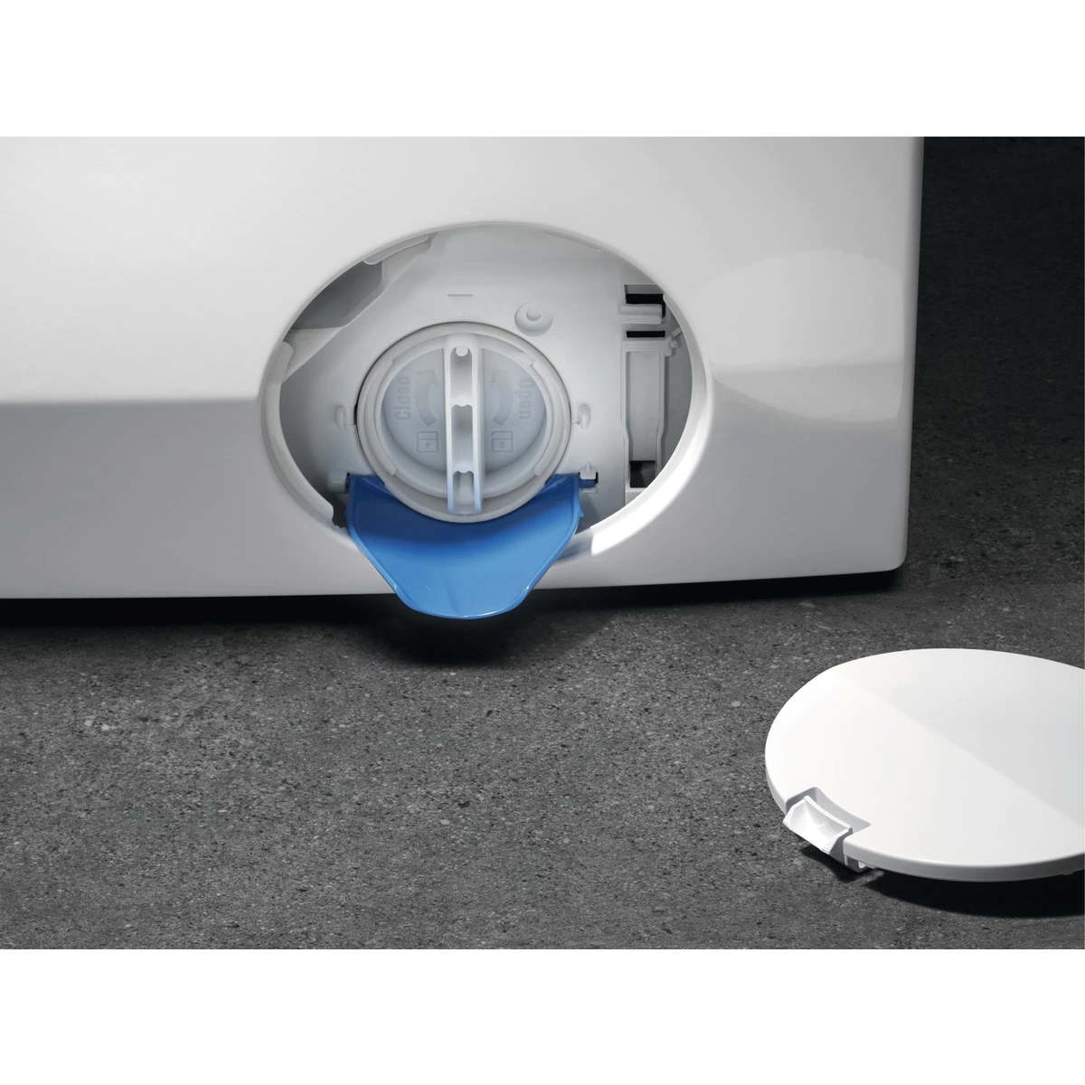 Biała pralka z otwartą niebieską pokrywą komory filtra na szarej podłodze.