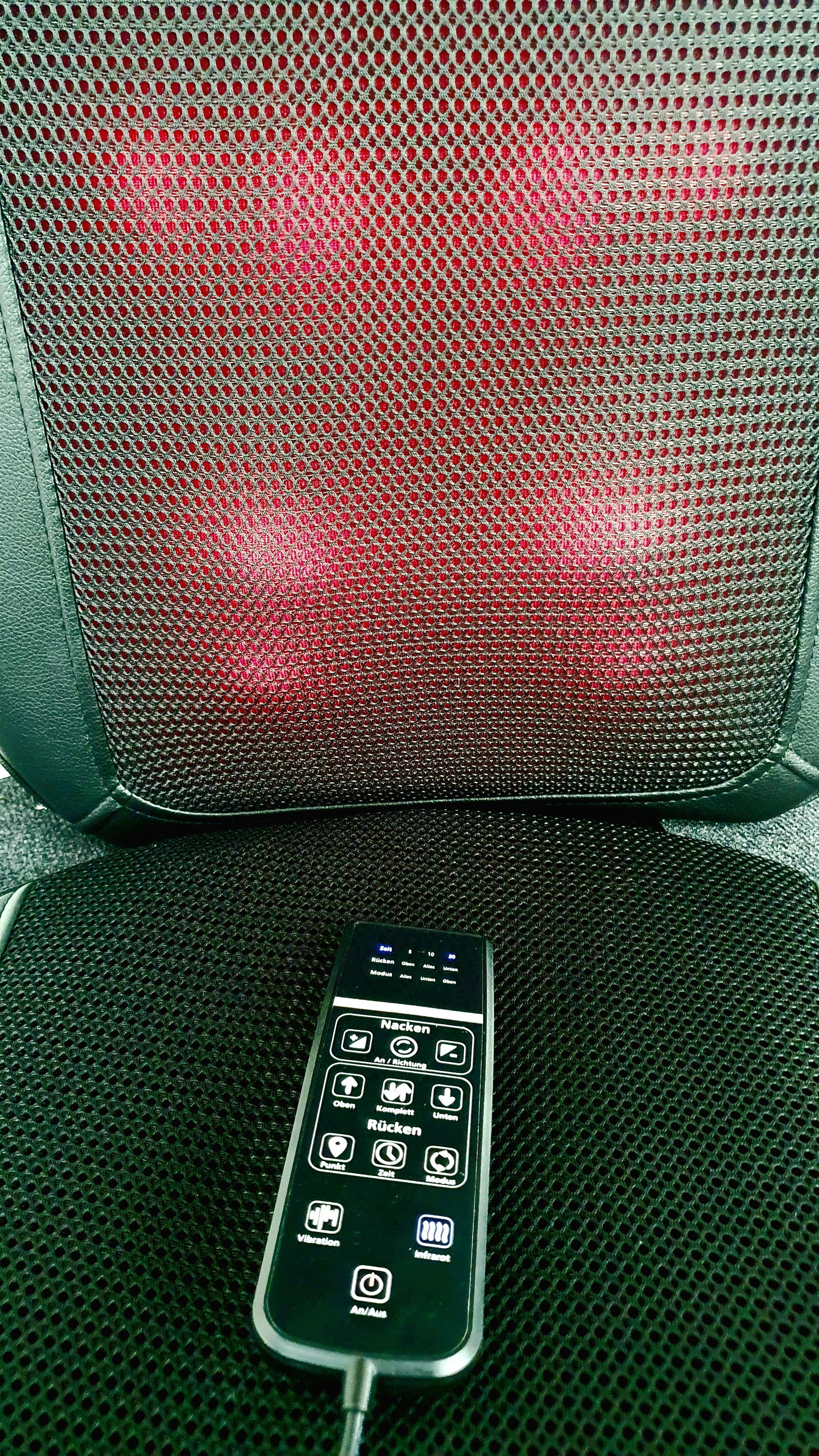 Ein Massagekissen mit Fernbedienung. Das Kissen ist schwarz mit roten Lichtern.