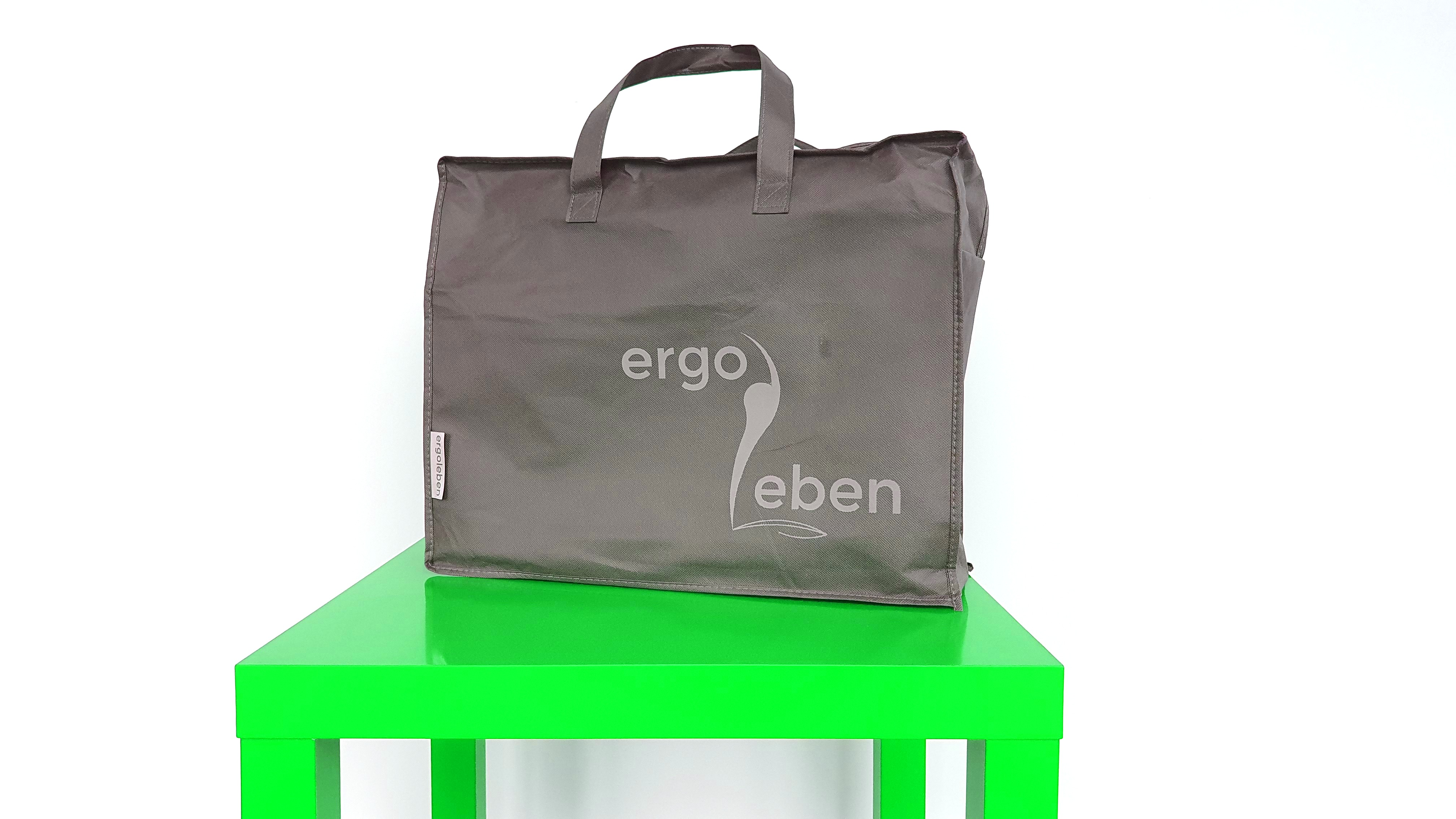 Graue Tragetasche mit der Aufschrift 'ergo leben' auf einem grünen Tisch.