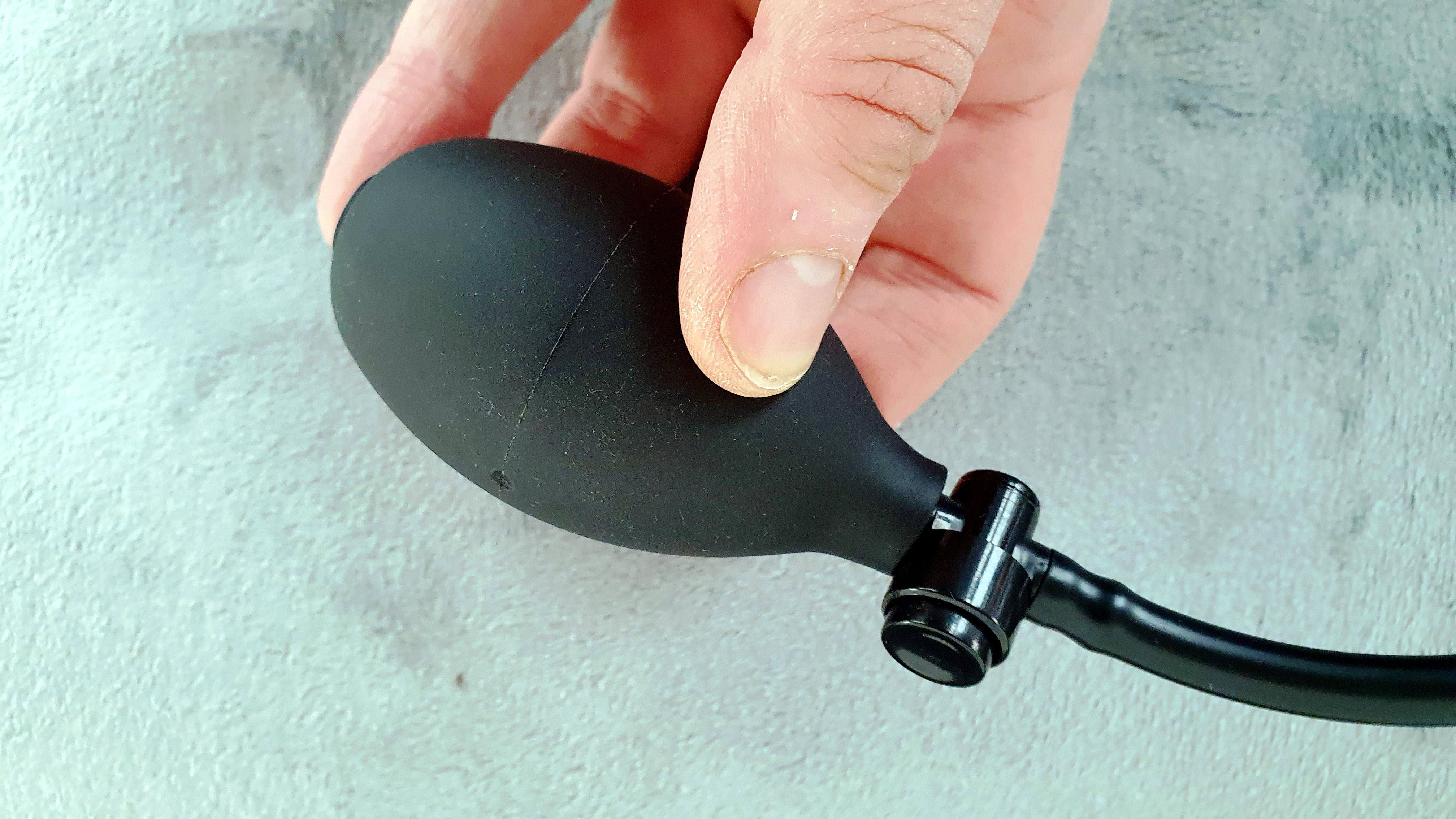 Eine Hand hält eine schwarze Ballonspritze. Die Spritze hat einen schwarzen Ball und einen schwarzen Schlauch.