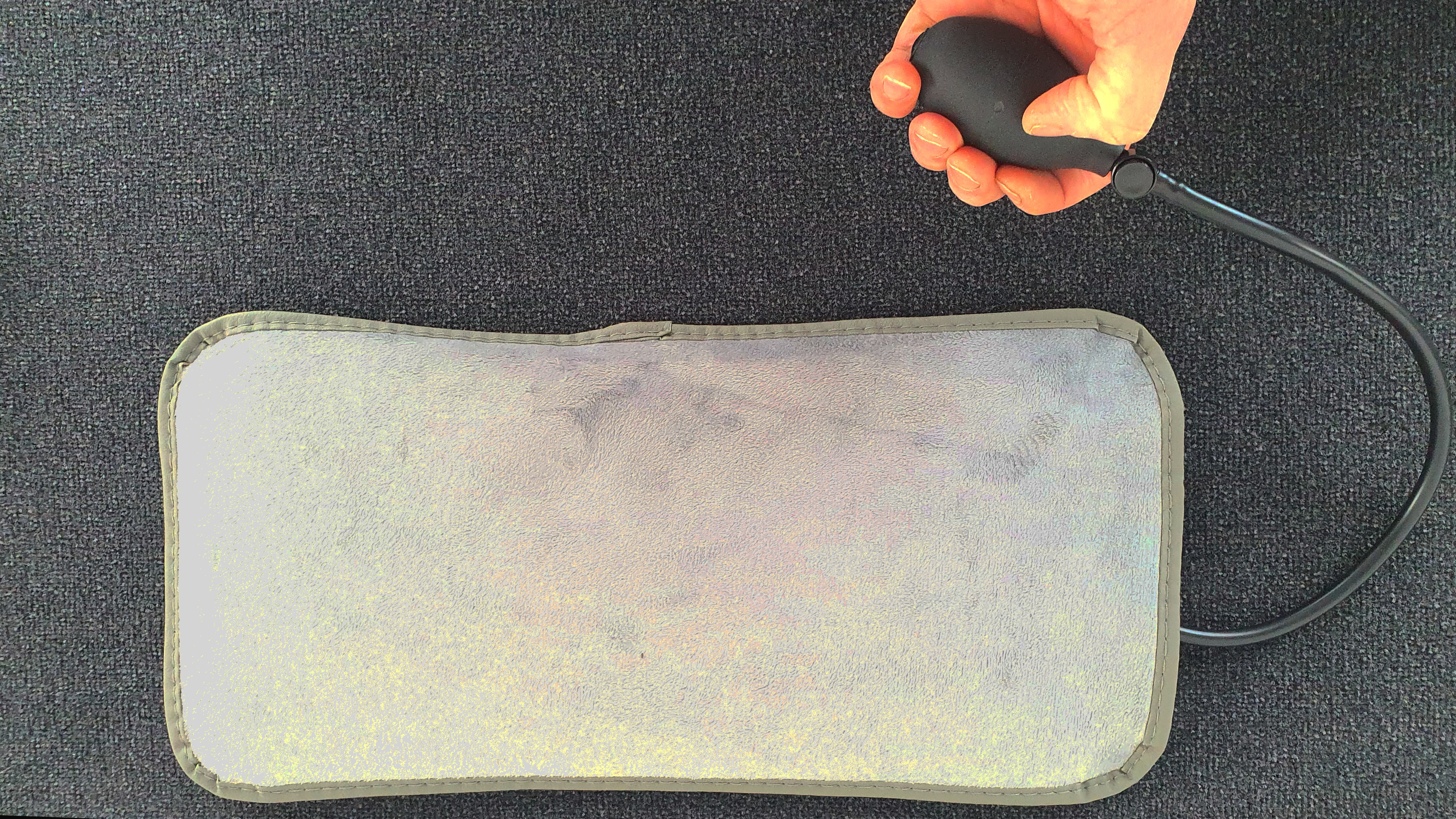 Ein graues Kissen, verbunden mit einer schwarzen Pumpe. Eine Hand hält die Pumpe, das Kissen liegt dunkel.