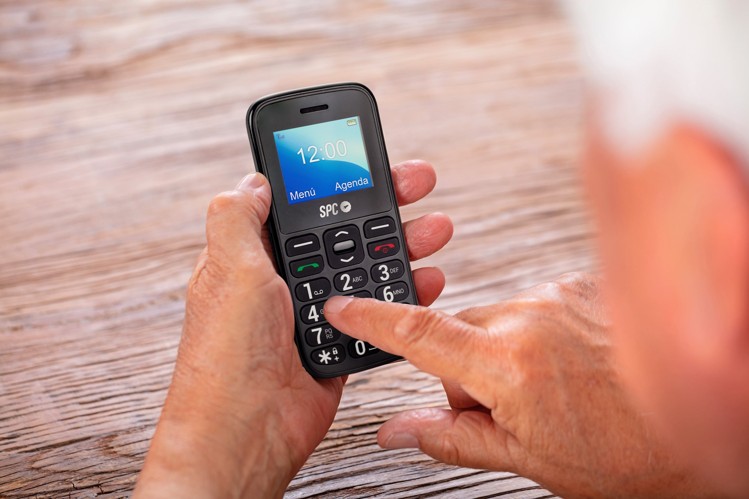 Hand hält einfaches Mobiltelefon, zeigt Zeit und Menüoptionen.