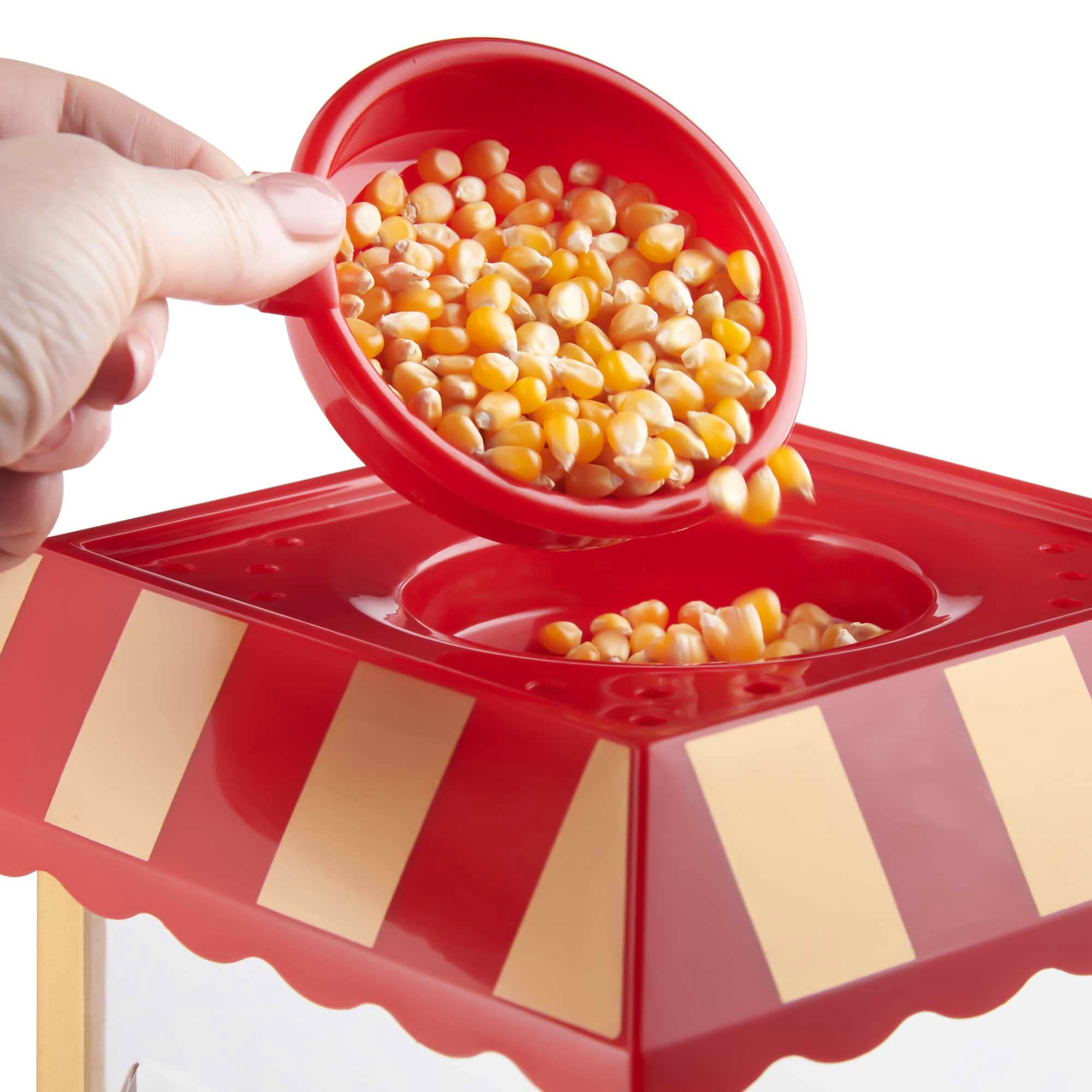 Mano vertiendo granos de palomitas en una máquina roja con parte superior a rayas.
