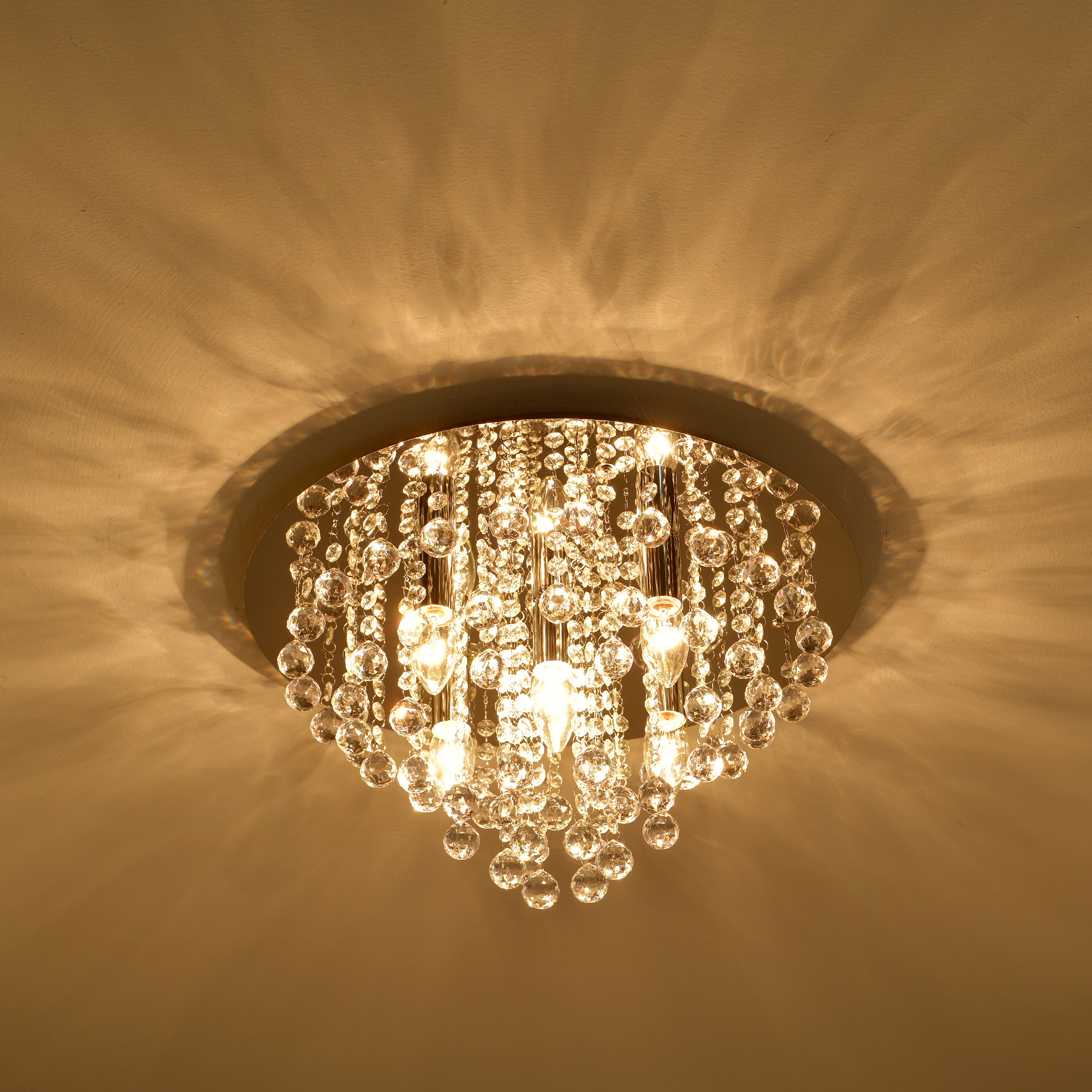 Ein runder Kronleuchter mit vielen Kristallperlen, der von einer weißen Decke hängt. Licht scheint.