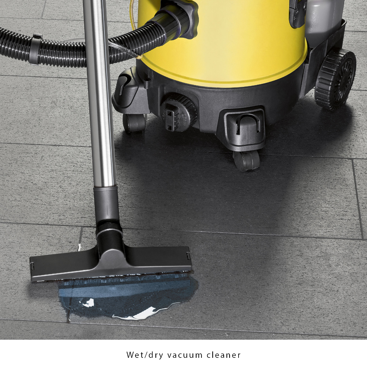Żółto-czarny odkurzacz na mokro na ciemnoszarej podłodze z płytek. Wąż i dysza są widoczne.
