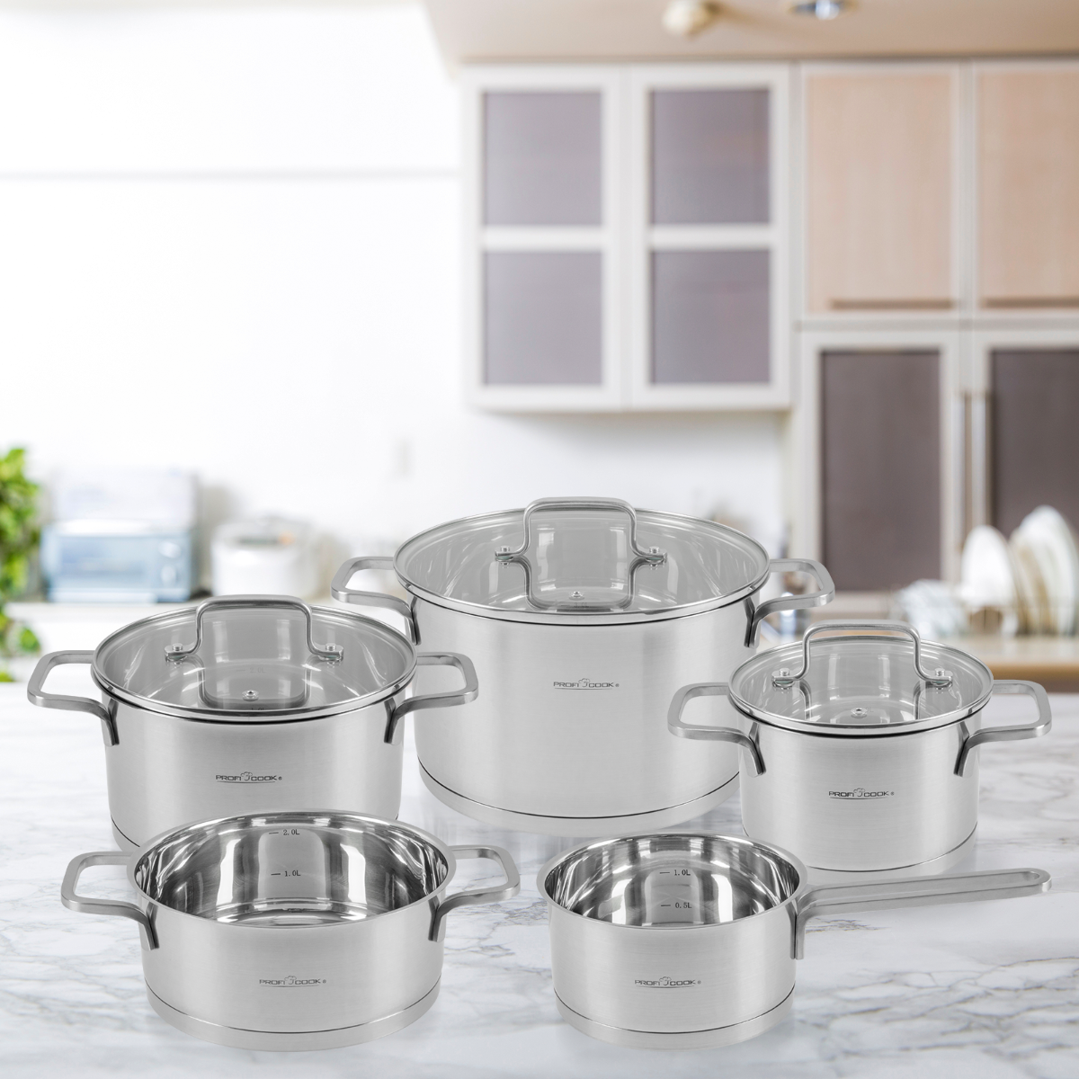 Zestaw garnków i patelni ze stali nierdzewnej ze szklanymi pokrywkami na marmurowym blacie w kuchni.