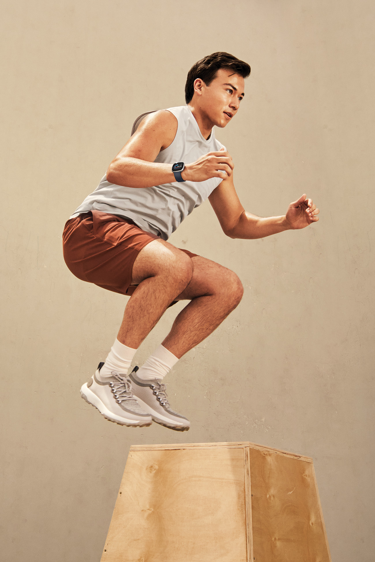 Mężczyzna skaczący na drewnianą skrzynię, ubrany w strój treningowy i zegarek fitness.