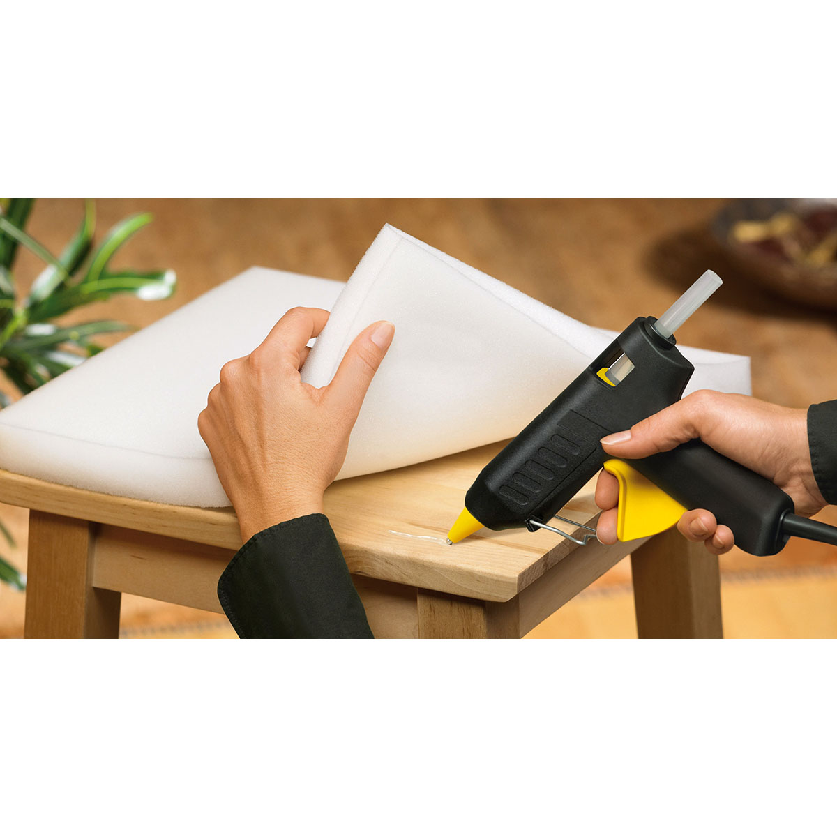 Person verwendet Klebepistole, um Schaumstoff an Hocker zu befestigen. Pistole ist schwarz-gelb.
